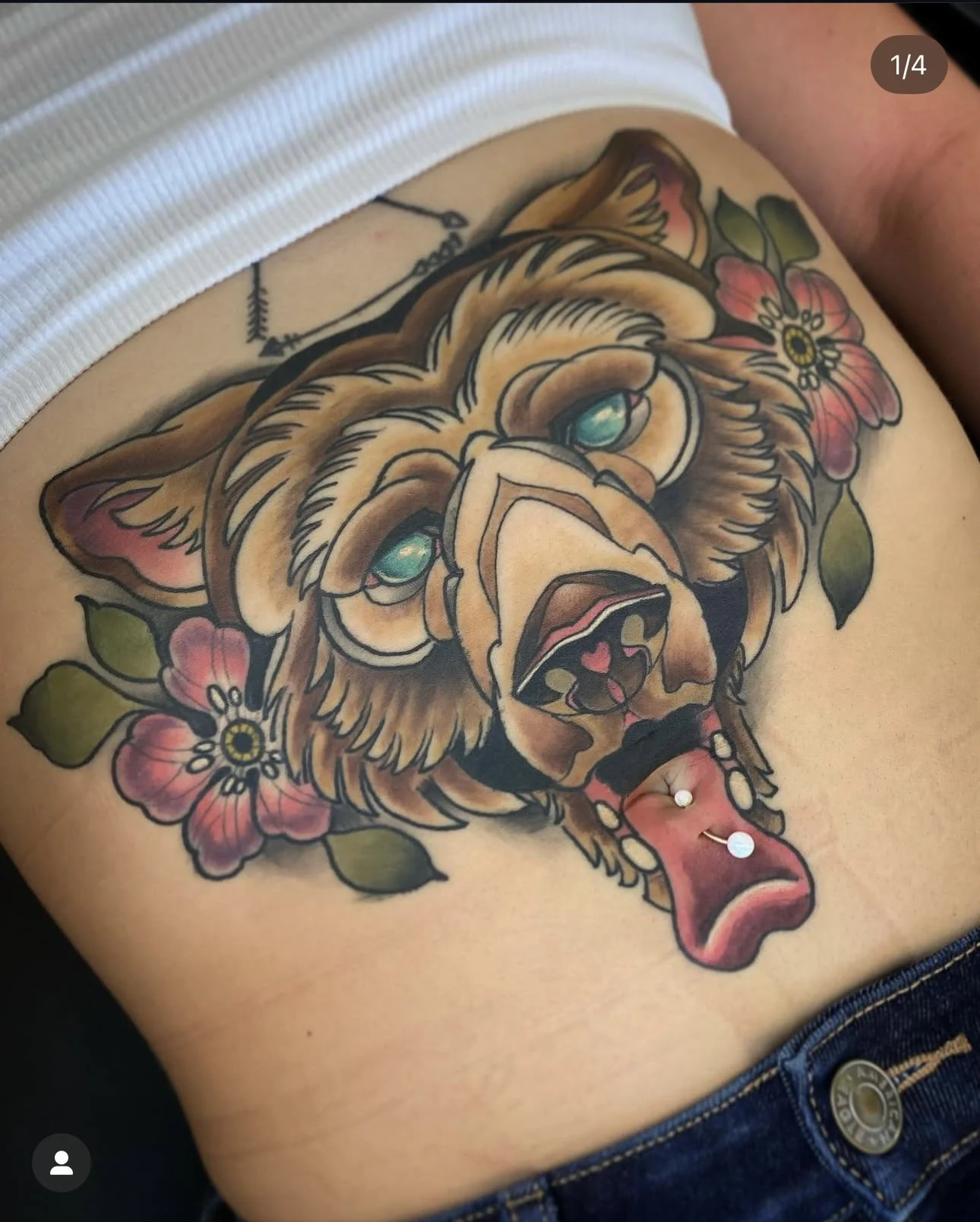 Colorful tattoo of a bear's head with blue eyes, surrounded by pink flowers and green leaves on person's side.