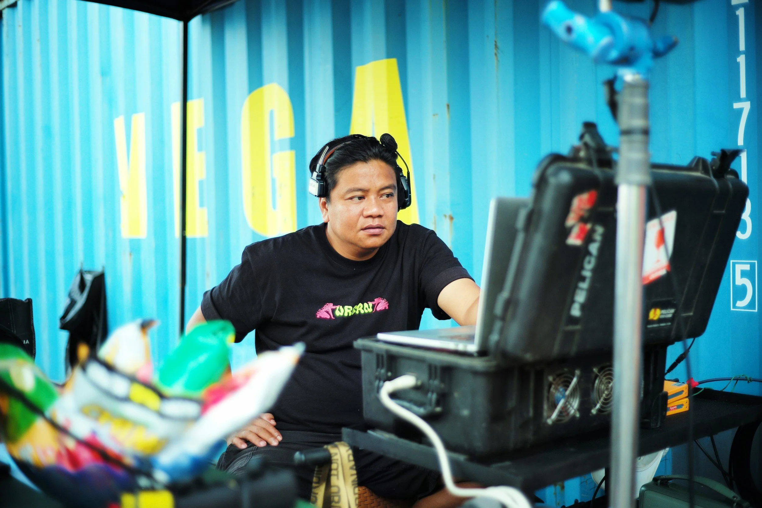 Man wearing headphones working on laptop in front of blue shipping containers with yellow and white lettering.