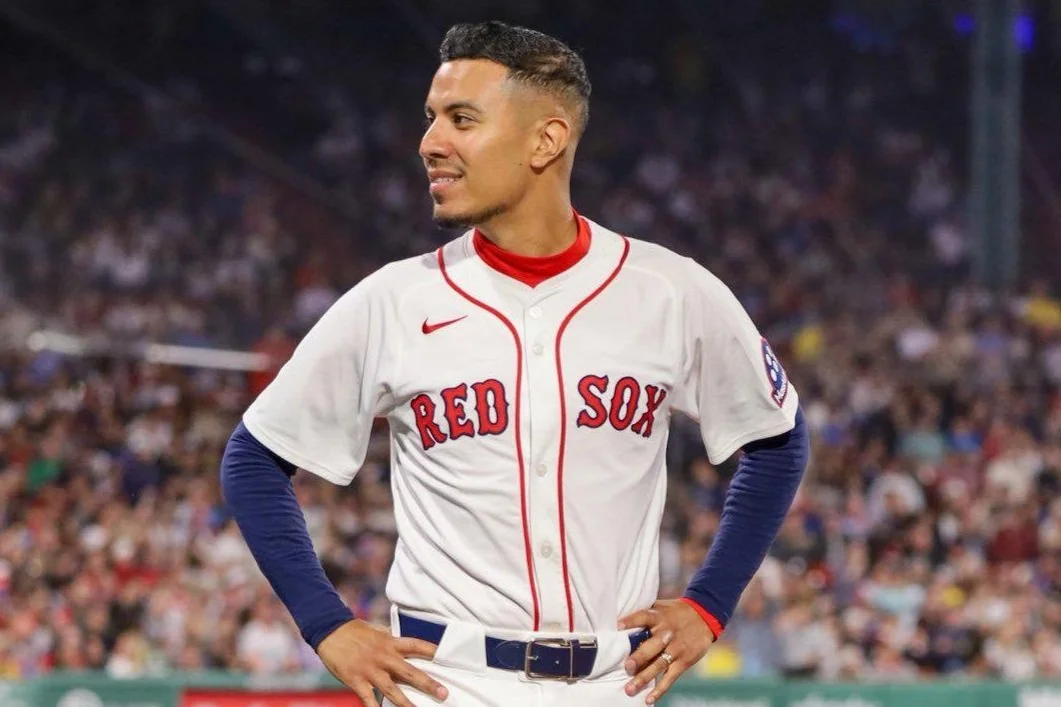 A baseball player from the Boston Red Sox standing on the field with hands on hips, in a stadium with a blurred crowd in the background.