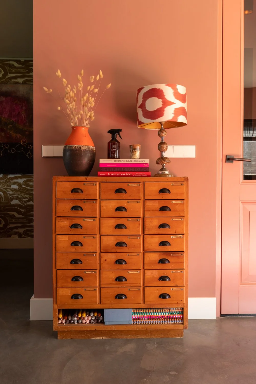 Kast met meerdere kleine laden, met decoratieve items en boeken op top tegen een roze muur