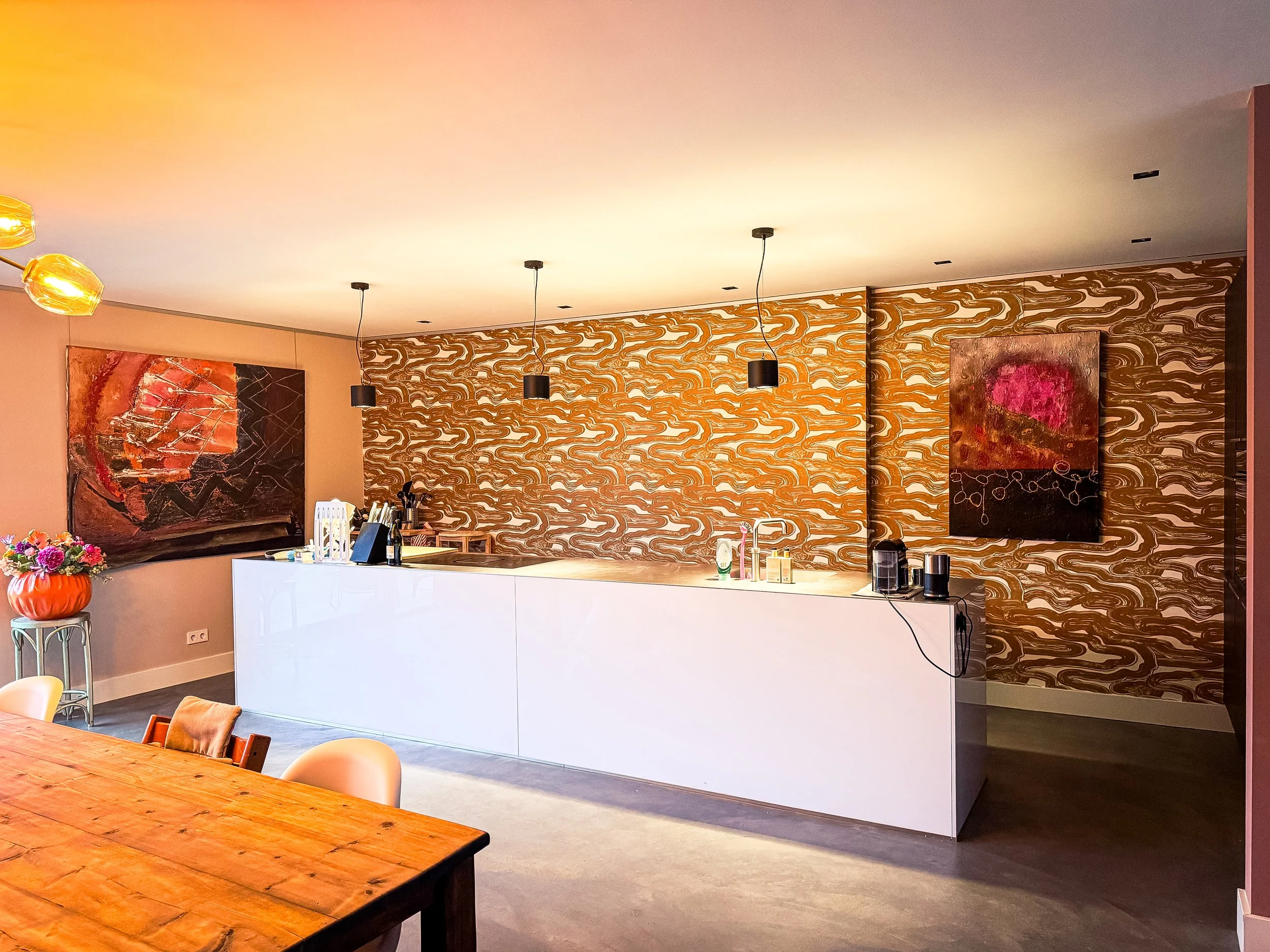 Modern keuken met een witte keukentafel, muurdecoraties en zwart verlichte plafondlampen.