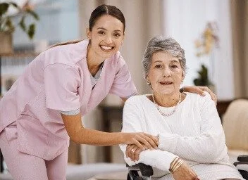 A young woman in pink scrubs caring for an elderly woman in a wheelchair