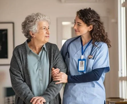 A nurse holding the arm of an elderly woman at a healthcare facility.