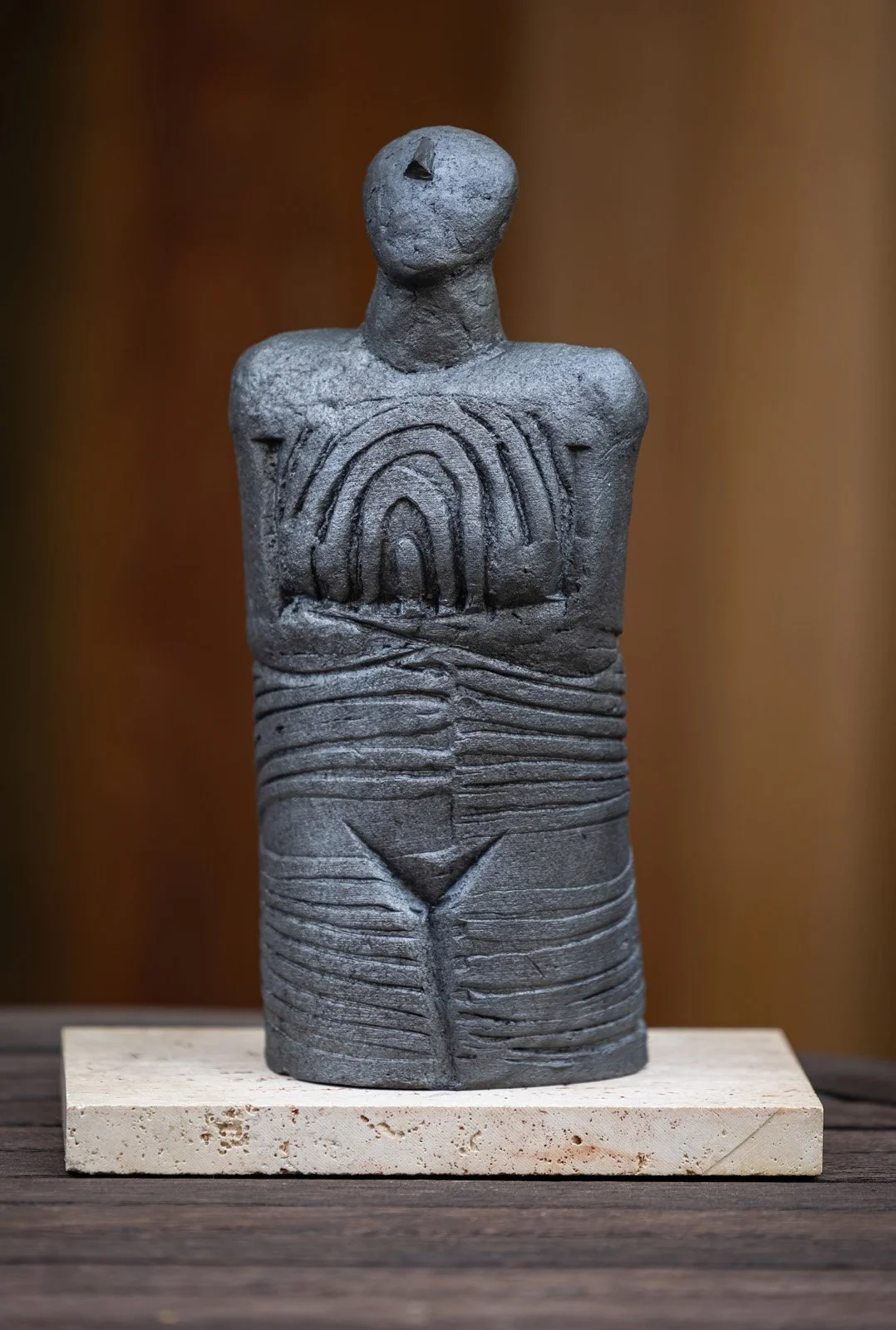 A clay sculpture of a human figure with geometric patterns on its torso, mounted on a wooden block.