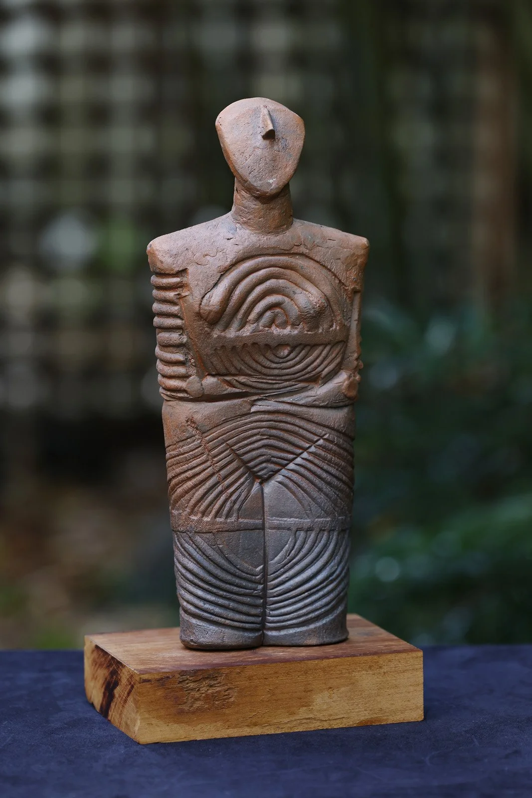 A clay sculpture of a human figure with geometric patterns on its torso, mounted on a wooden block.