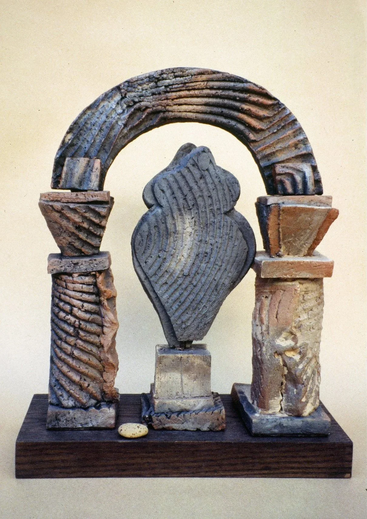 A clay sculpture of ancient-style architecture with four columns, an arch, and a central decorative element on a wooden base.