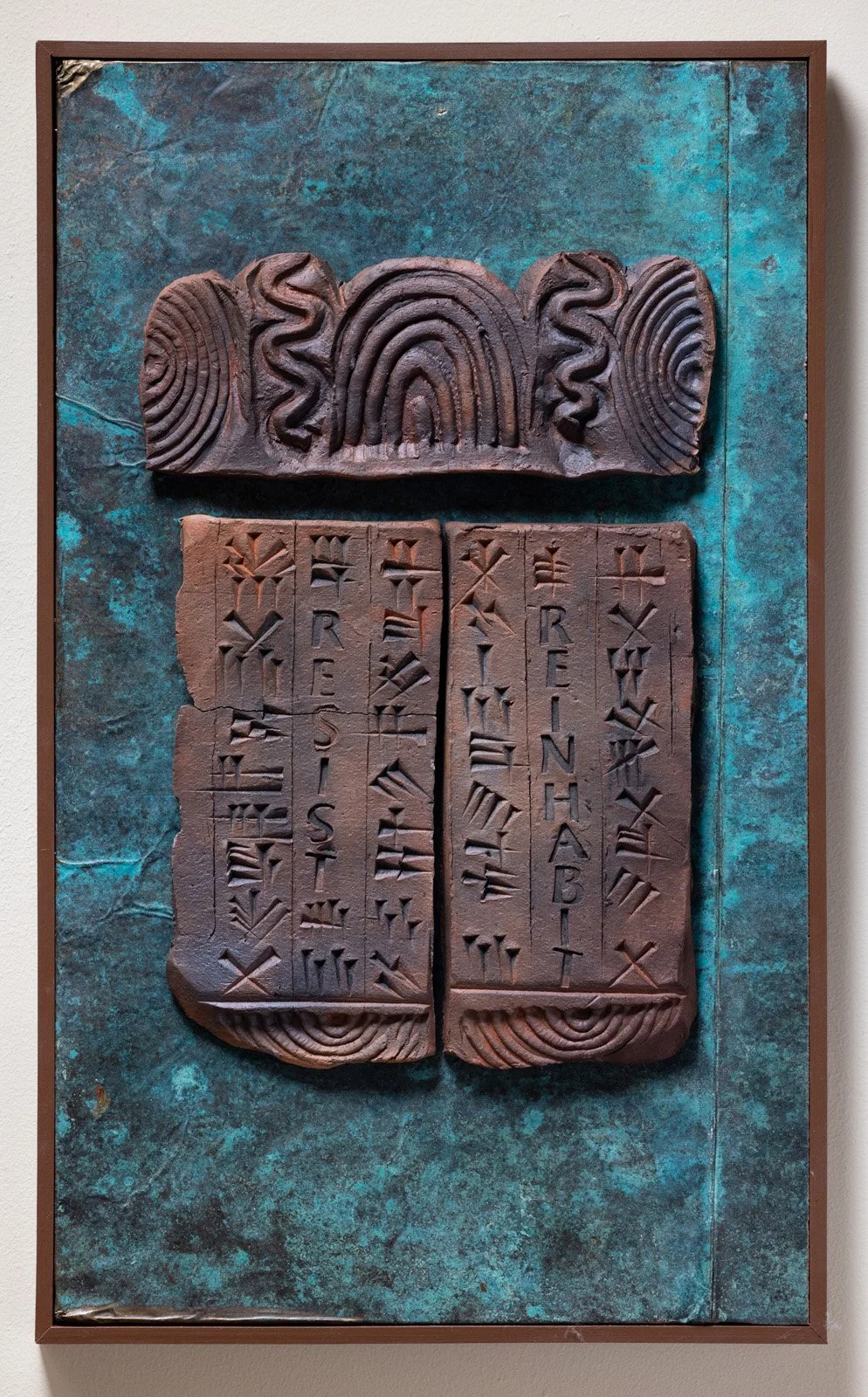 Clay tablets with inscriptions and abstract patterns mounted on a textured, teal background.