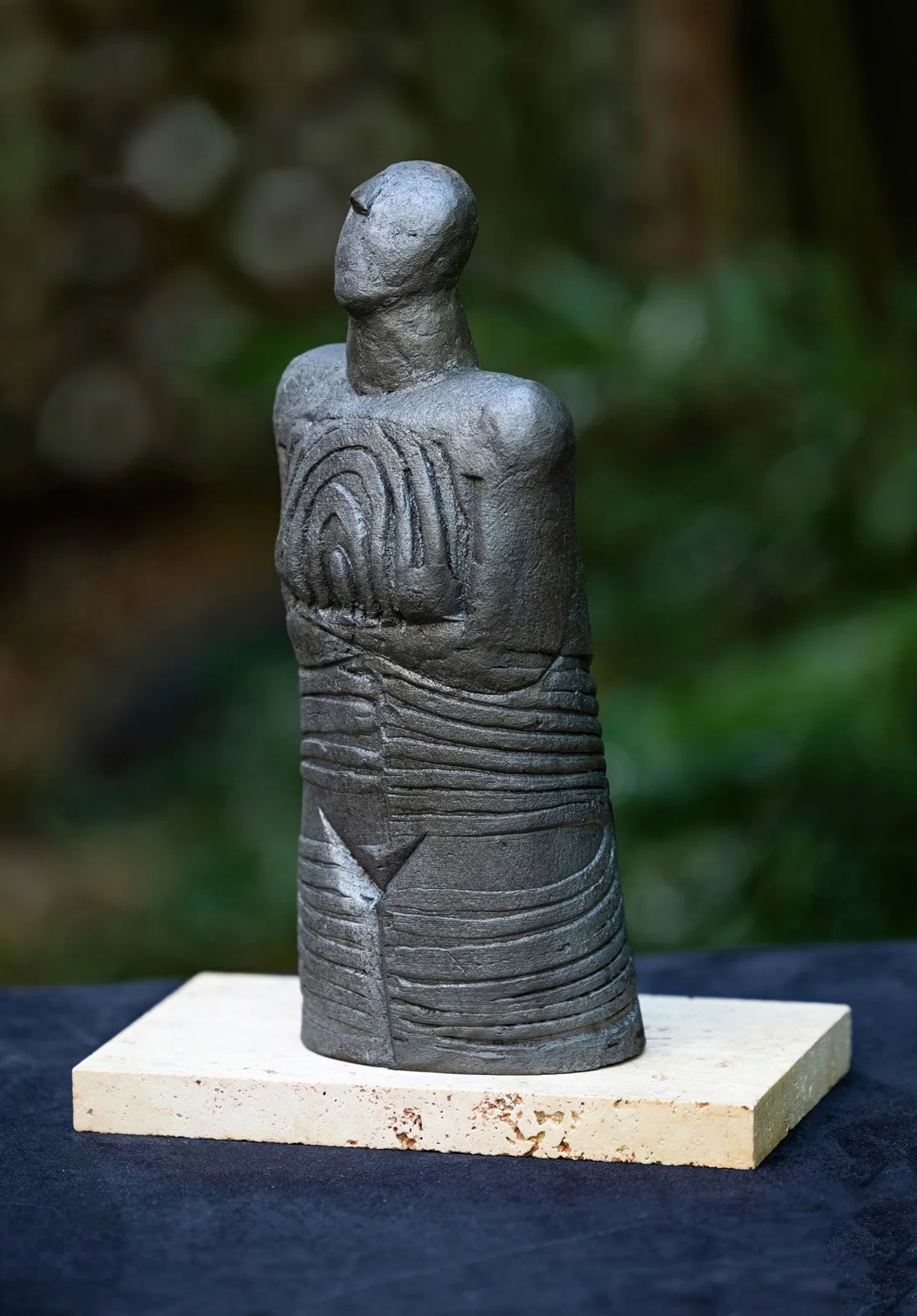 A clay sculpture of a human figure with geometric patterns on its torso, mounted on a wooden block.