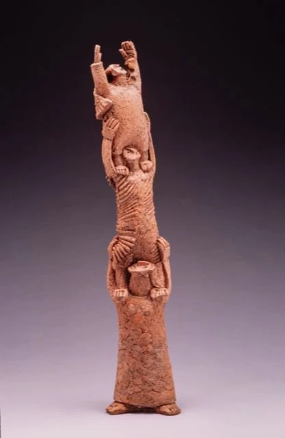A tall, reddish-brown ceramic sculpture of intertwined human figures.