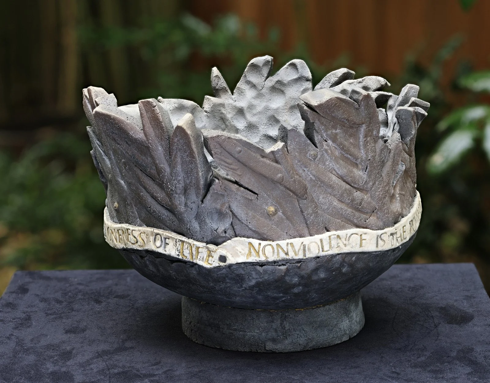 A clay sculpture shaped like a large bowl, with a banner wrapping around the base that reads 'NONVIOLENCE OF LIFE.'