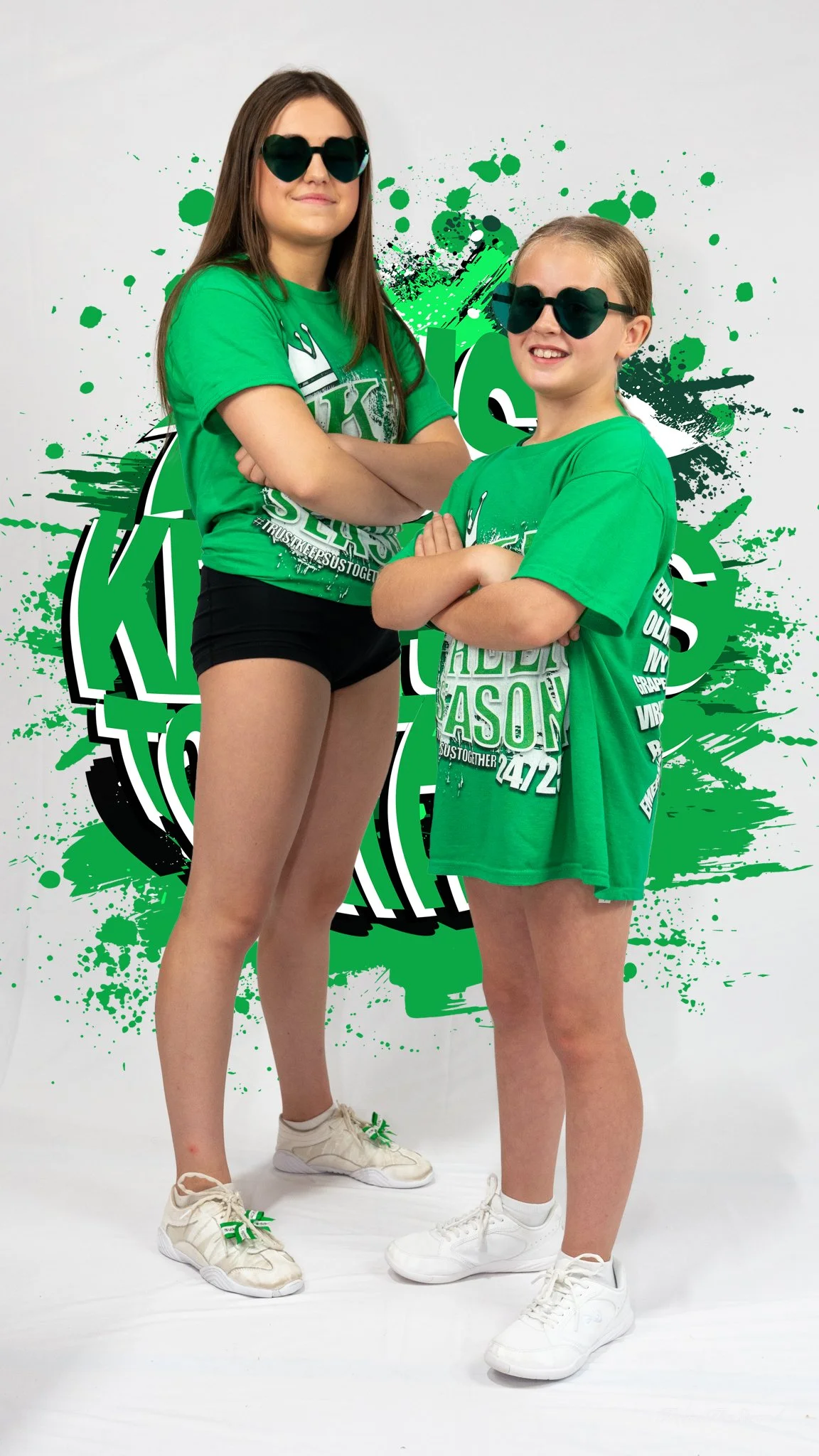 Two girls wearing green T-shirts and sunglasses standing in front of a green and black graphic background.