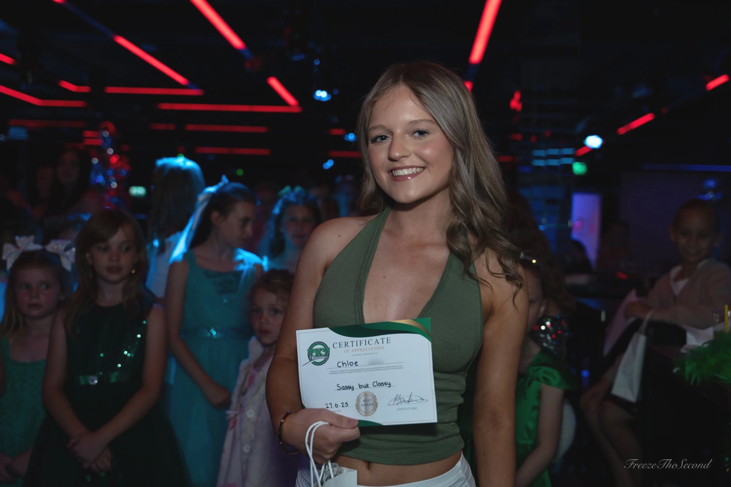 Cheerleaders performing a routine, wearing green and white uniforms with 'TKT' on the front, at a cheerleading competition.