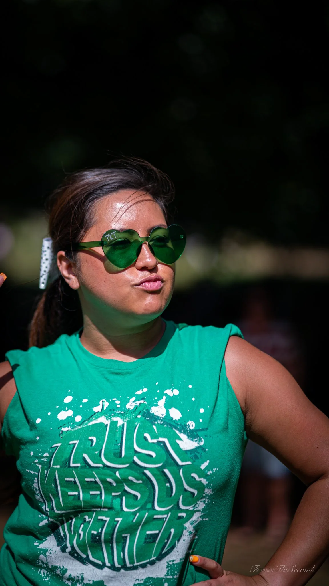 Woman wearing green sunglasses and sleeveless green shirt with a graphic print, outdoors on sunny day