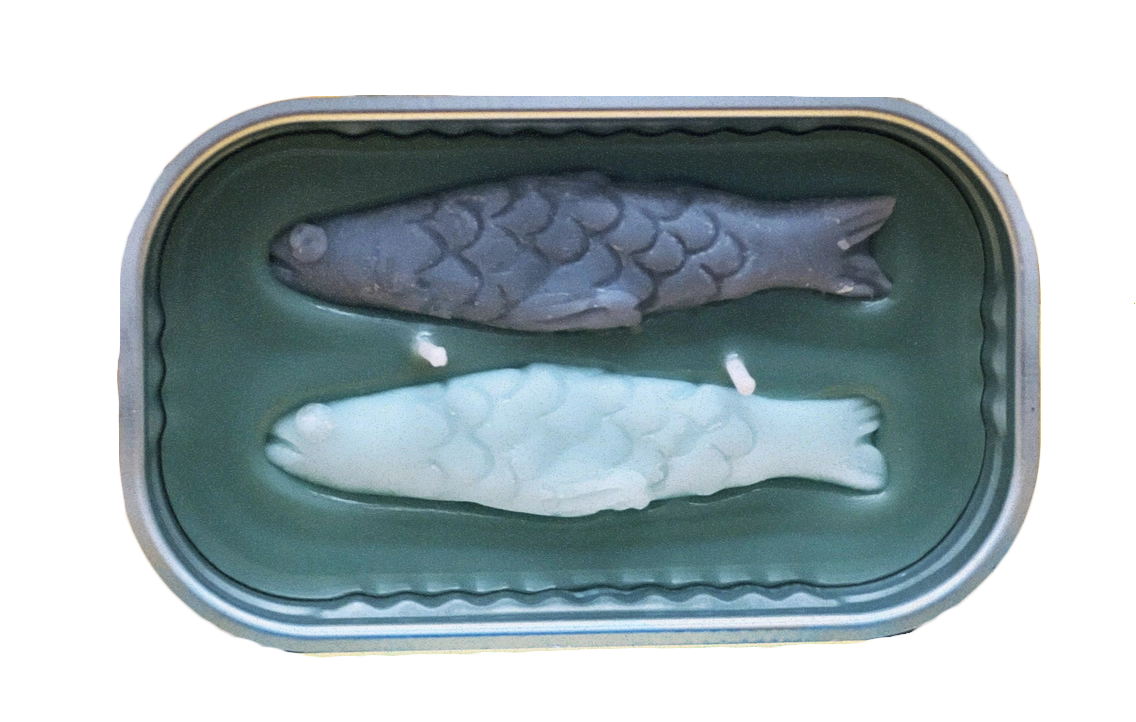Candle with Two fish, one black and one white, inside an opened can of fish. Not edible.
