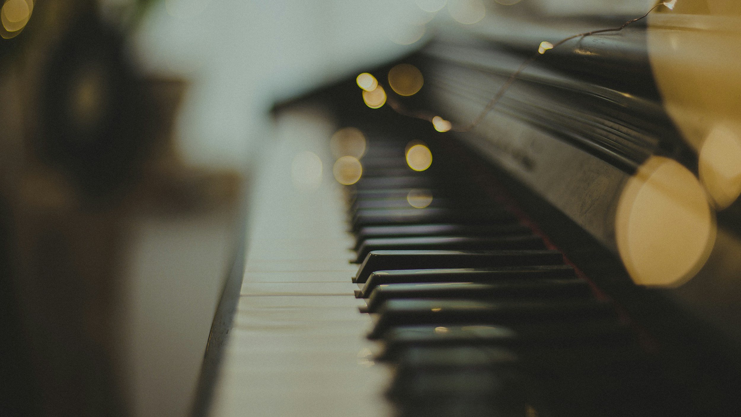 Close-up of a piano keyboard with a blurred background of piano keys and some bokeh lights.