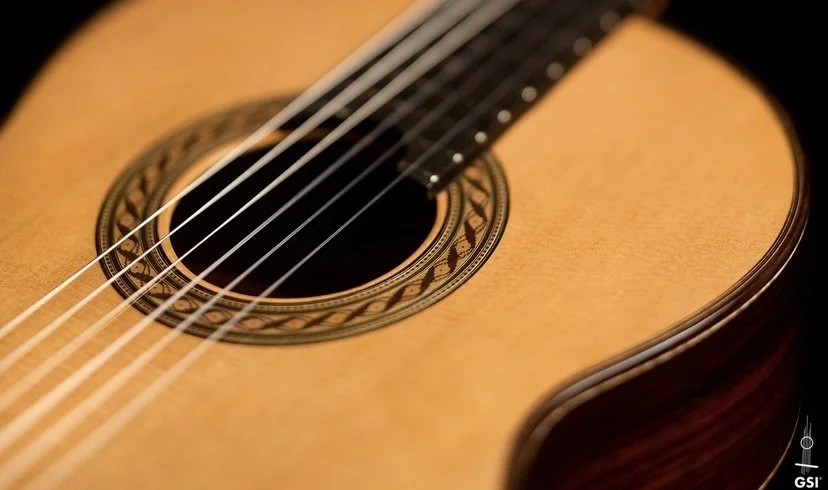 Close-up of an acoustic guitar's soundhole, strings, and wooden body with decorative rosette pattern.