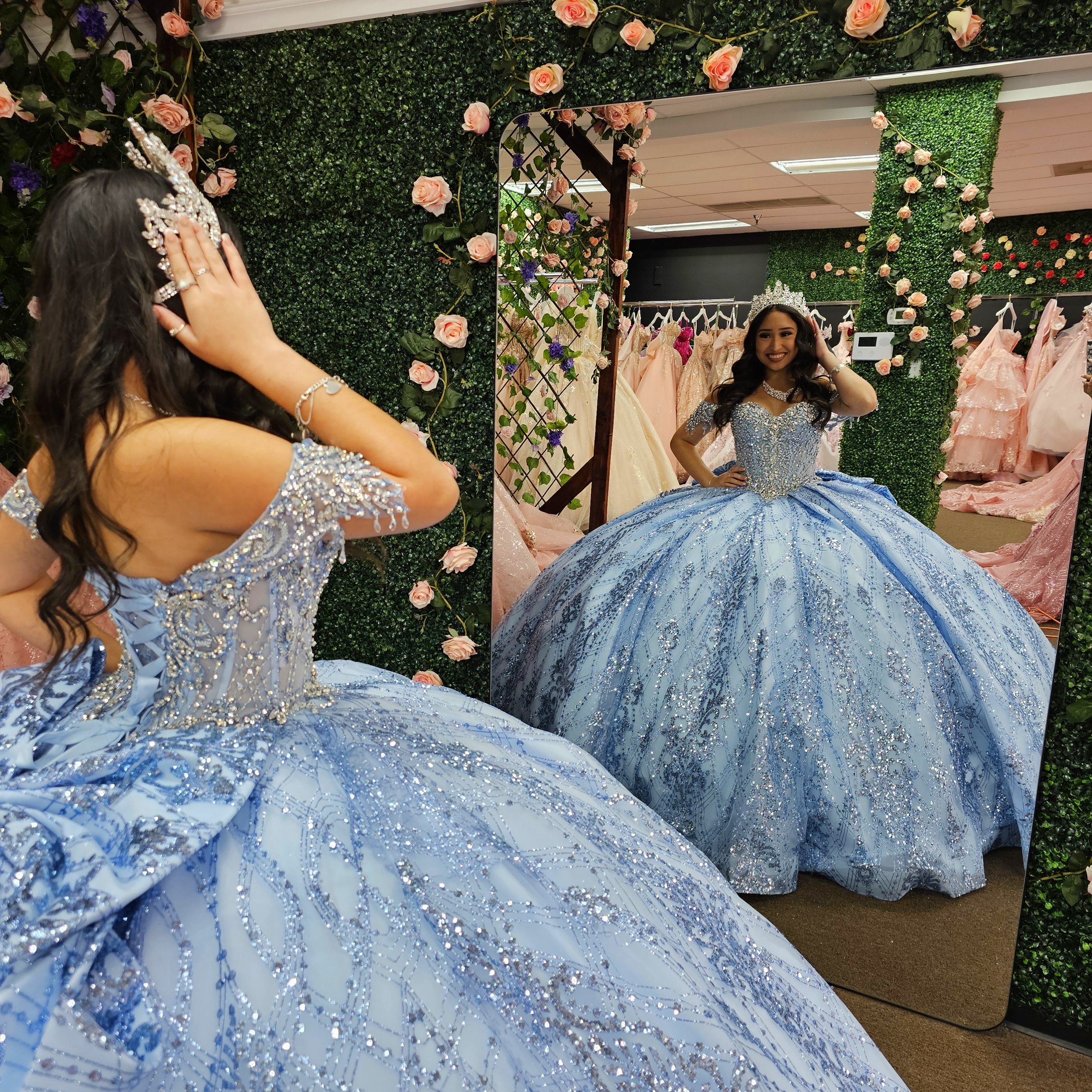 Young woman trying on a light cinderella blue quince with silver embellishments in Quinceaneras and Bridals boutique, looking at herself in a mirror.