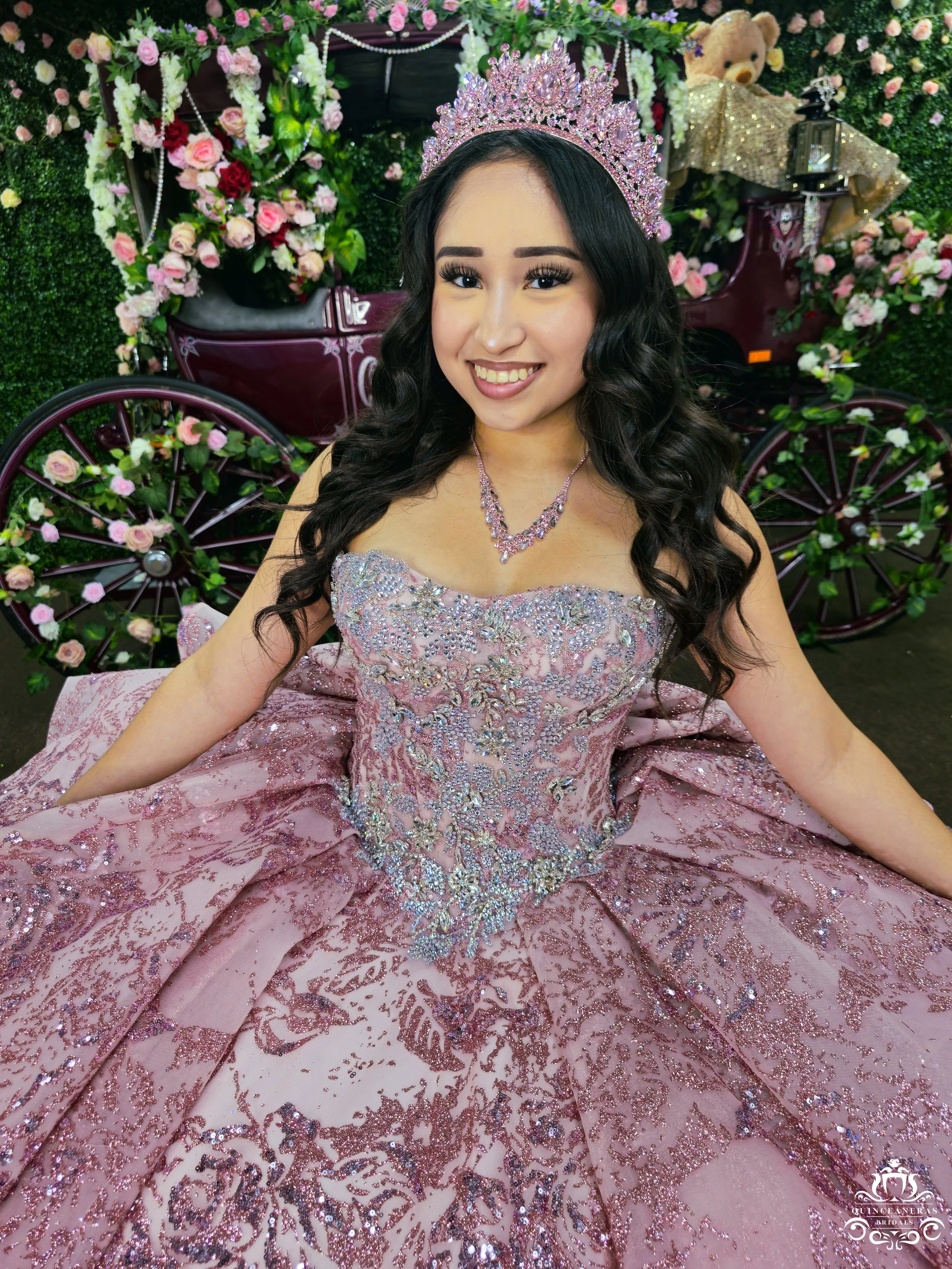 A young woman wearing a sparkly pink quince dress and a pink tiara, sitting in front of Quinceaneras and Bridals boutique's signature carriage in San Antonio, Texas. 