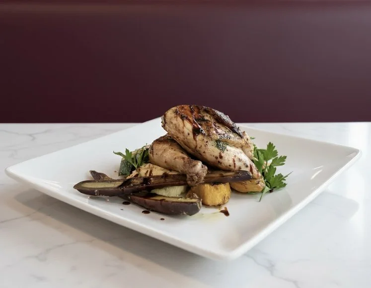 Grilled chicken breast with eggplant, potatoes, and herbs on a white square plate.