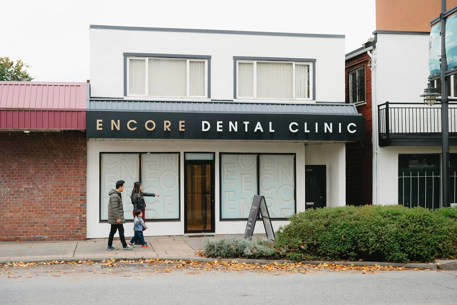 Exterior view of Encore Dental Clinic storefront with three people walking on sidewalk in front.