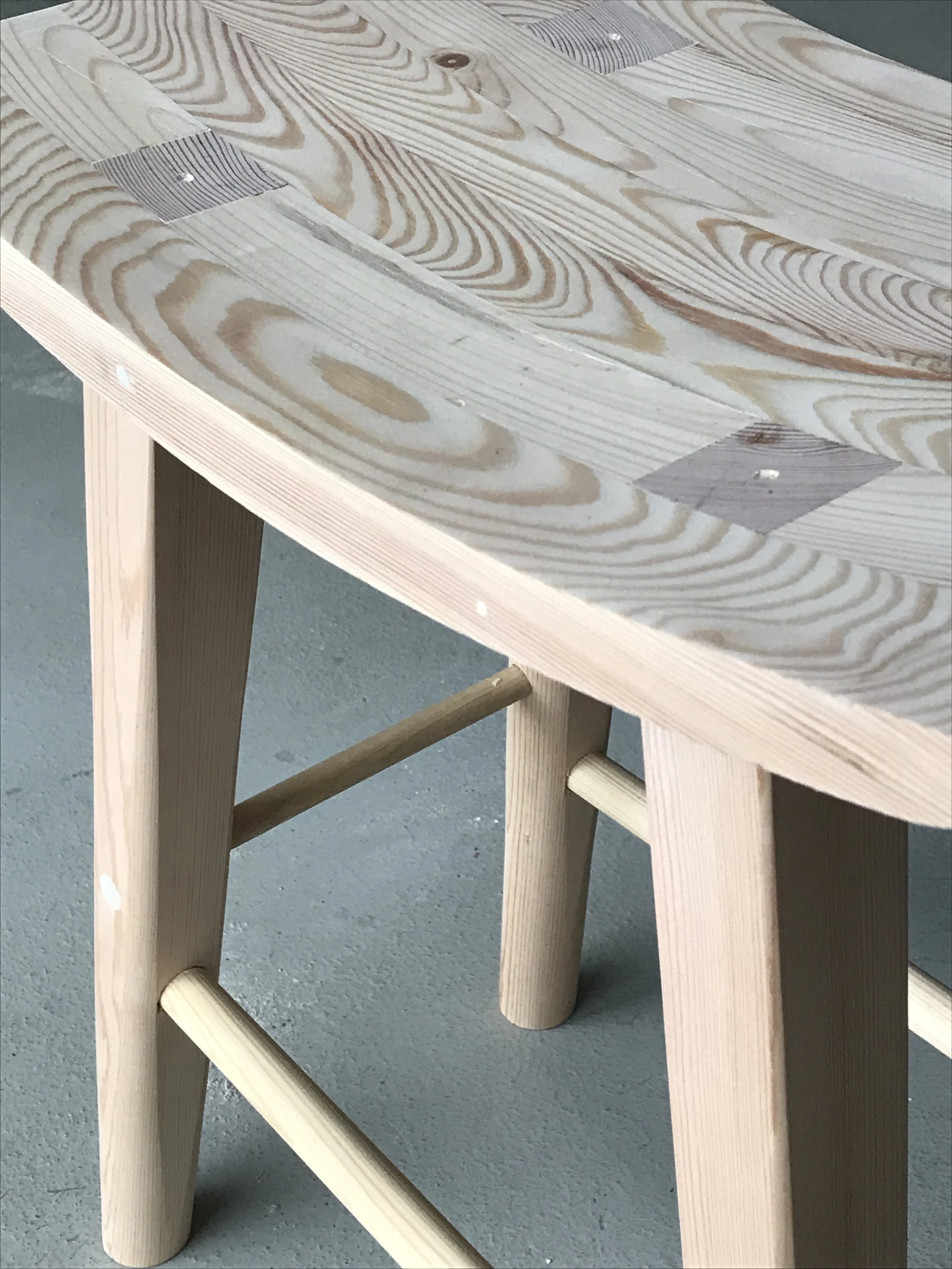 A wooden table with a light, natural finish and visible wood grain, supported by angled legs and a crossbar brace.