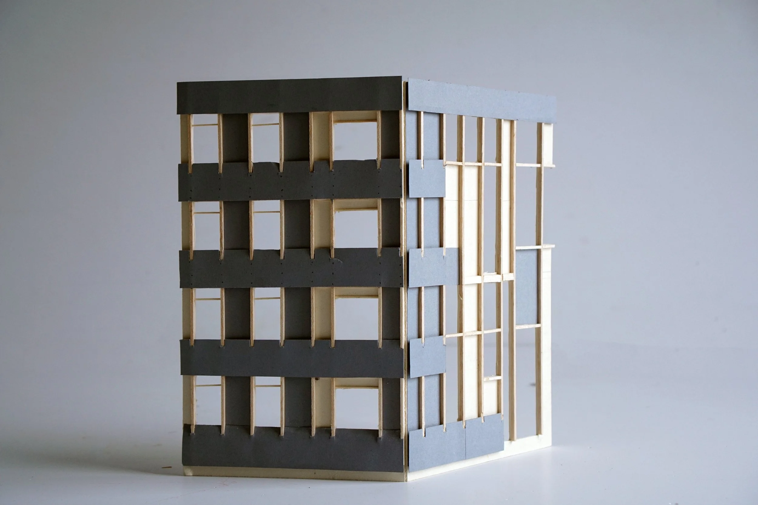 A model of a multi-story building framework made of wooden sticks and gray foam walls.