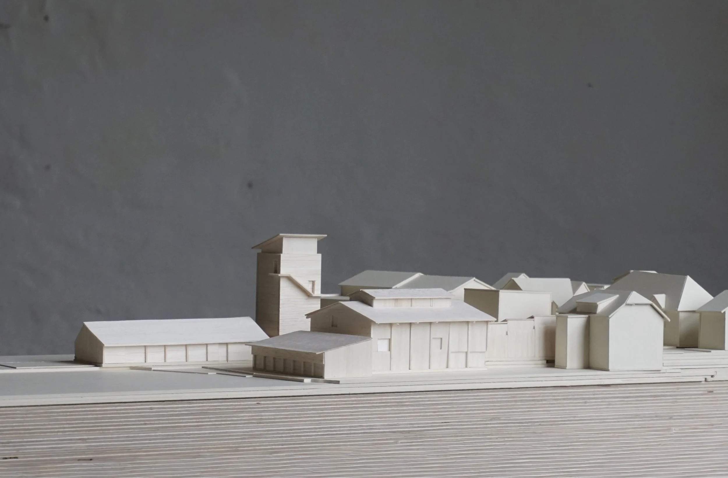 A detailed architectural model of a complex building with multiple structures, including a tall tower, set on a layered base with a textured background.