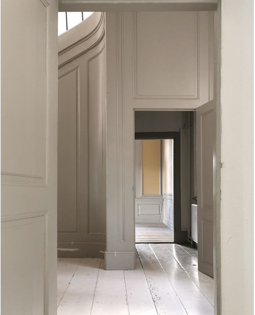 A view through multiple open doorways in a building showcasing white walls with decorative molding and wooden flooring.