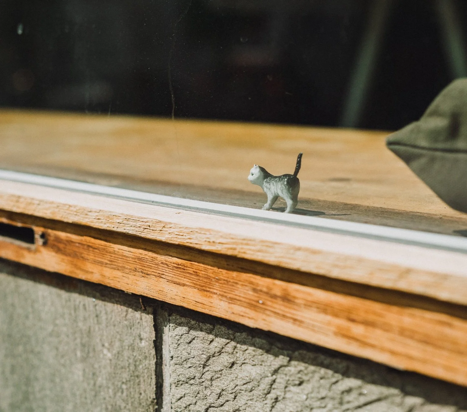 Small toy cat figurine placed on a wooden window sill with a glass window.