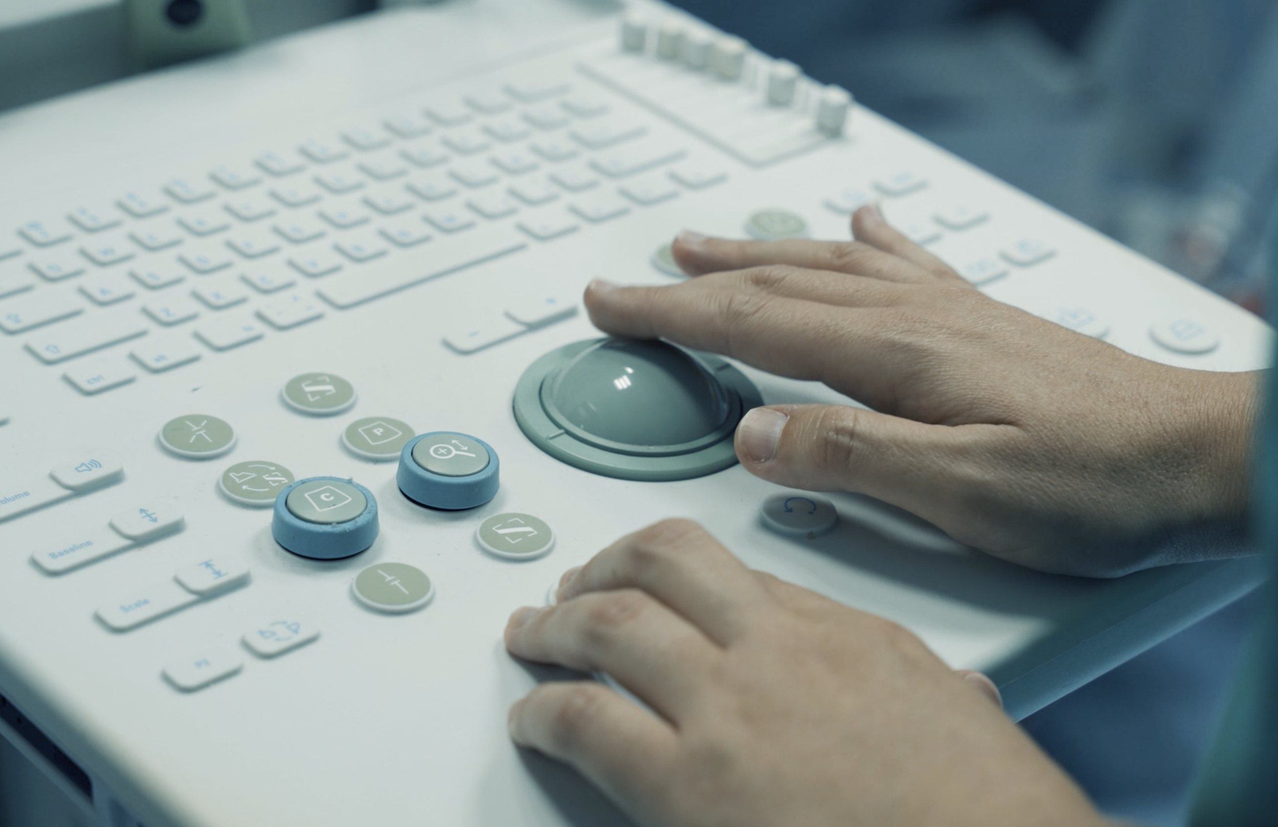 Una persona utilizza una macchina telefonica o di comunicazione con pulsanti blu e lucidi, e una tastiera con numeri e simboli, probabilmente in ambito sanitario.