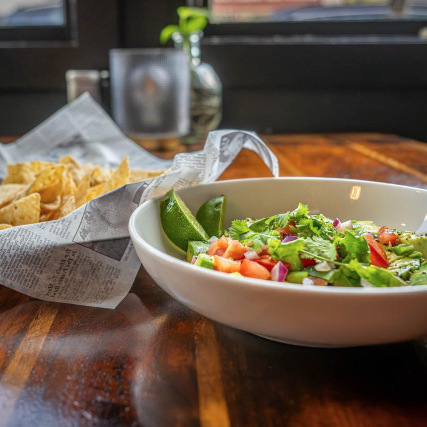 A bowl of fresh guacamole, served on a wooden table, accompanied by tortilla chips on newspaper.