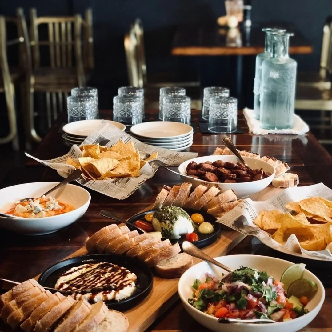 A table set with various dishes including bread, chips, a salad, and appetizers in a restaurant with drinking glasses and a water pitcher in the background.