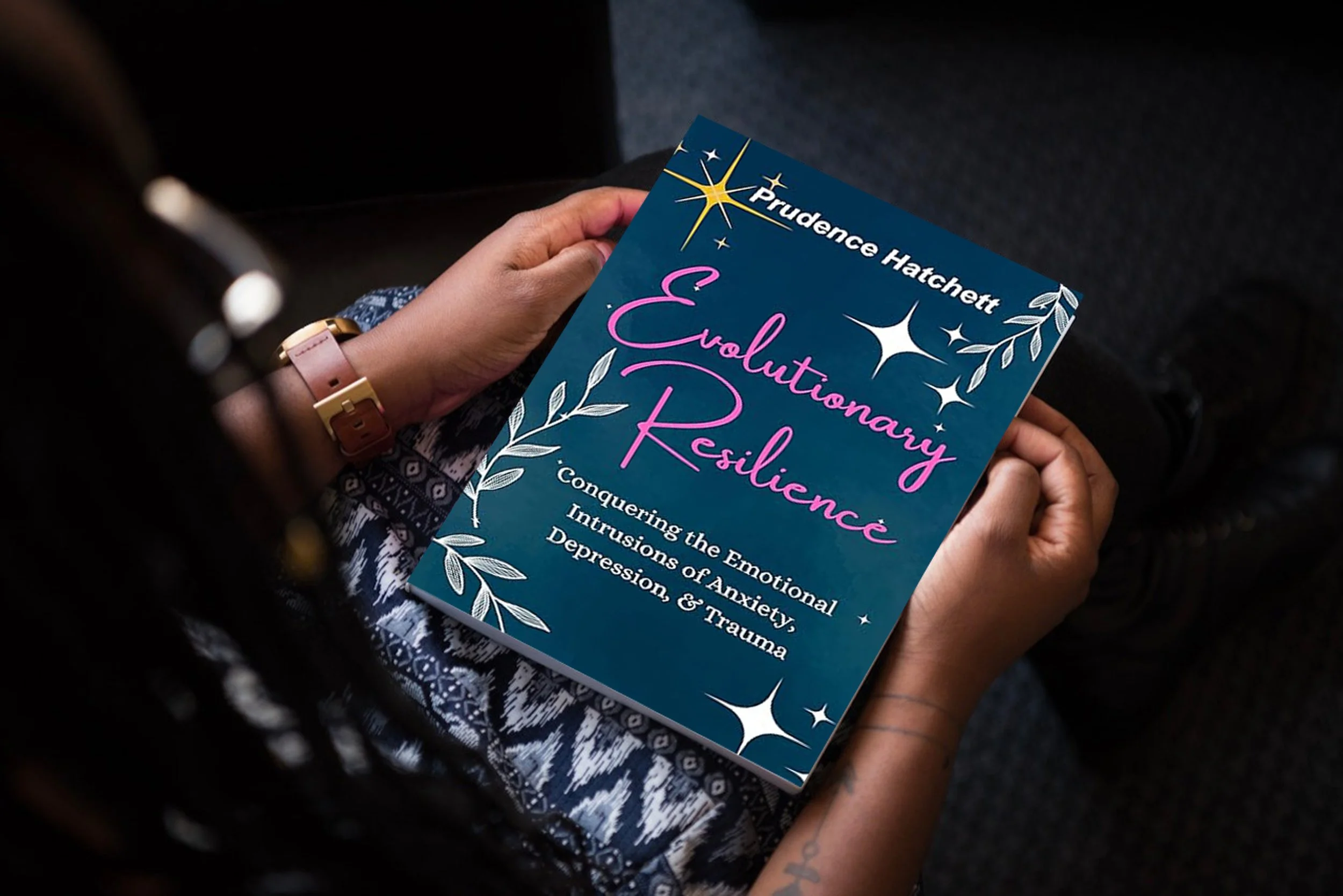 A person holding a book titled "Evolutionary Resilience" by Prudence Hatchett, with the subtitle "Conquering the Emotional Intrusions of Anxiety, Depression, & Trauma". The book cover is blue with decorative stars and leaves.