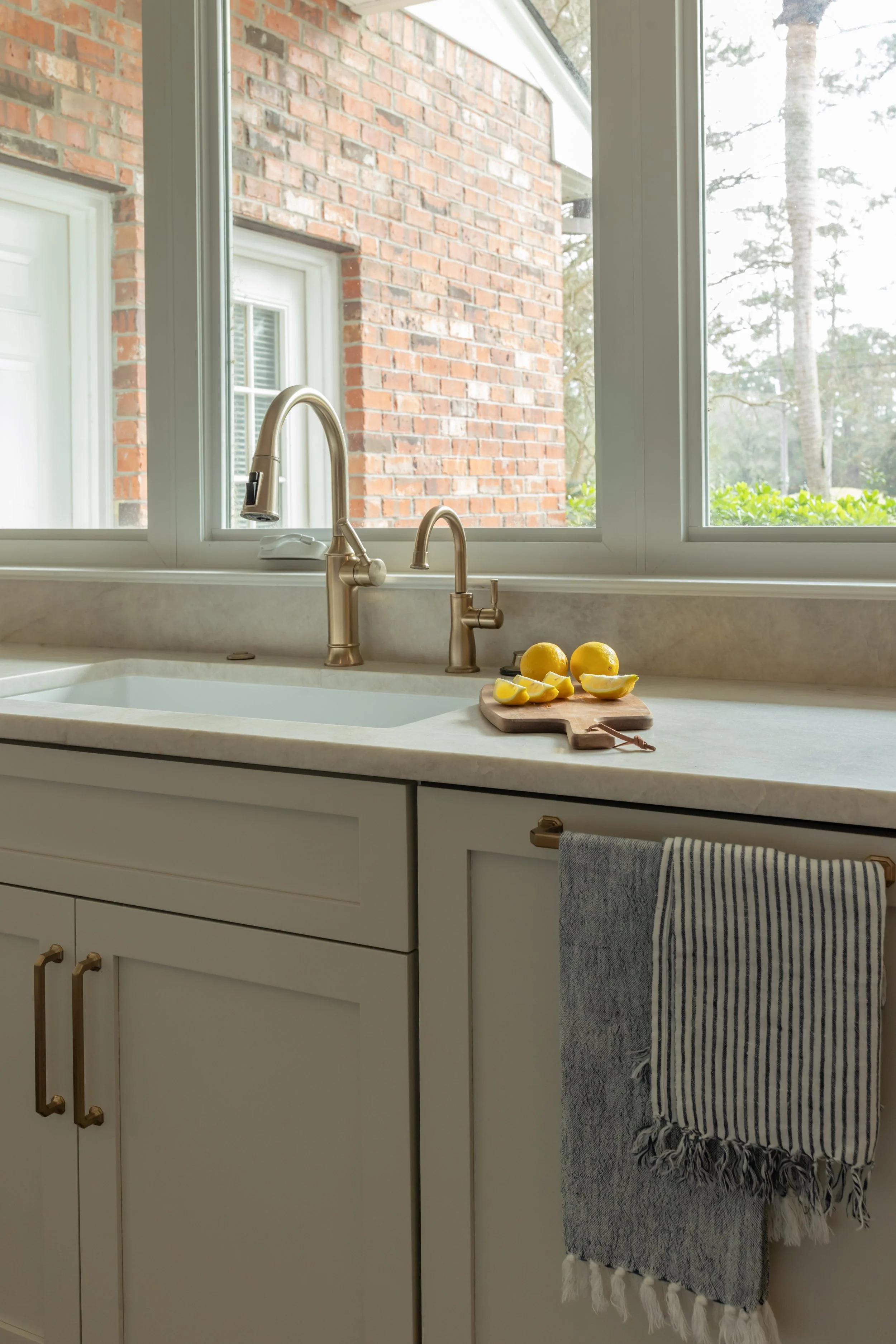 An undermount kitchen sink sits beneath the window, framed by pale stone countertops that reflect light throughout the room. The streamlined faucet adds a subtle shine while maintaining a clean, functional look.