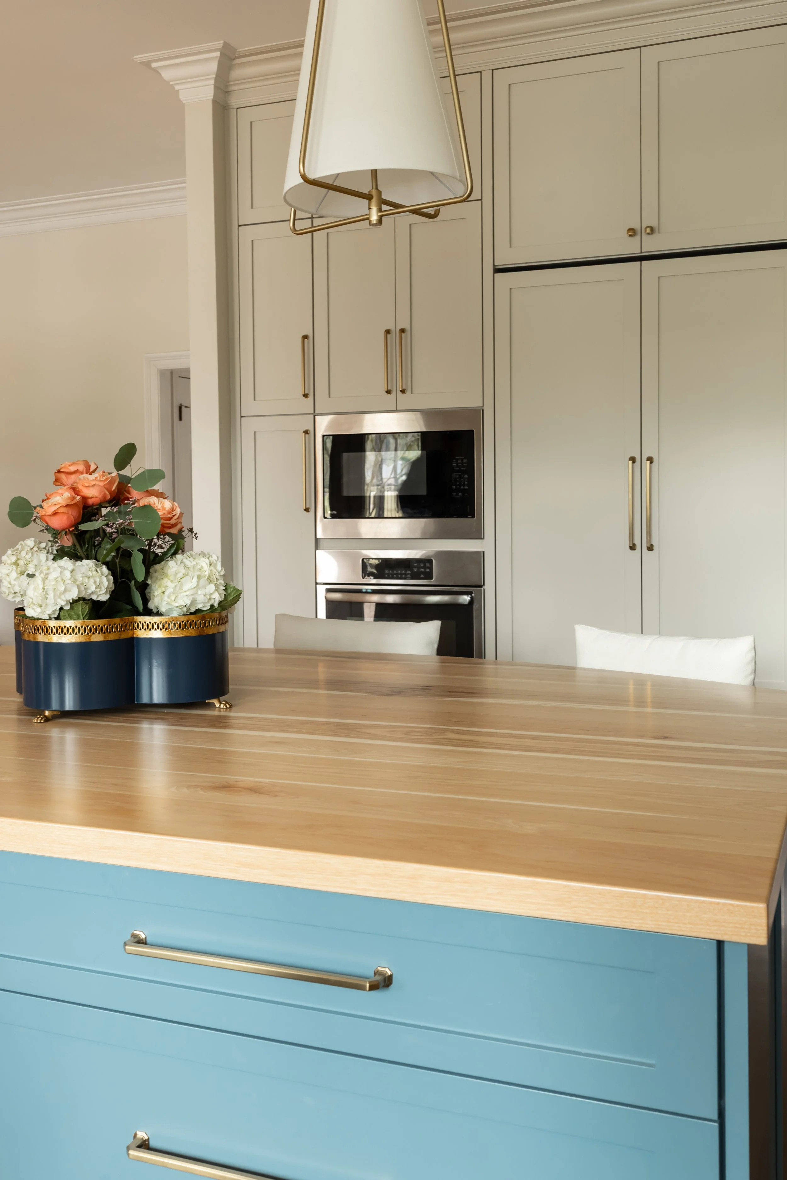 The custom kitchen island is painted a saturated blue, grounding the space and creating a bold focal point against the surrounding light cabinetry. A thick butcher block countertop introduces warmth and natural wood grain, inviting gathering, prep, a