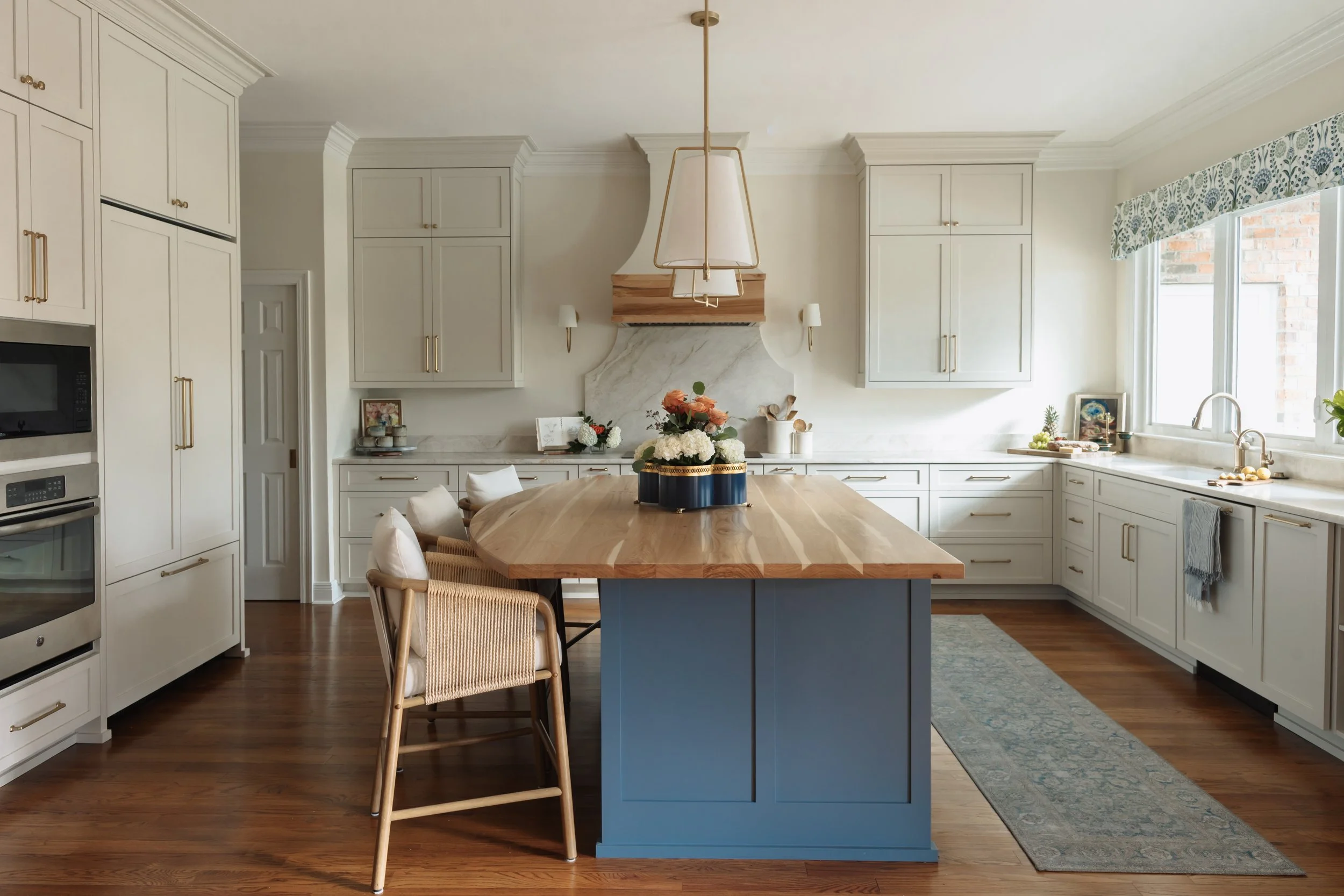 The custom kitchen island is painted a saturated blue, grounding the space and creating a bold focal point against the surrounding light cabinetry. A thick butcher block countertop introduces warmth and natural wood grain, inviting gathering, prep, a