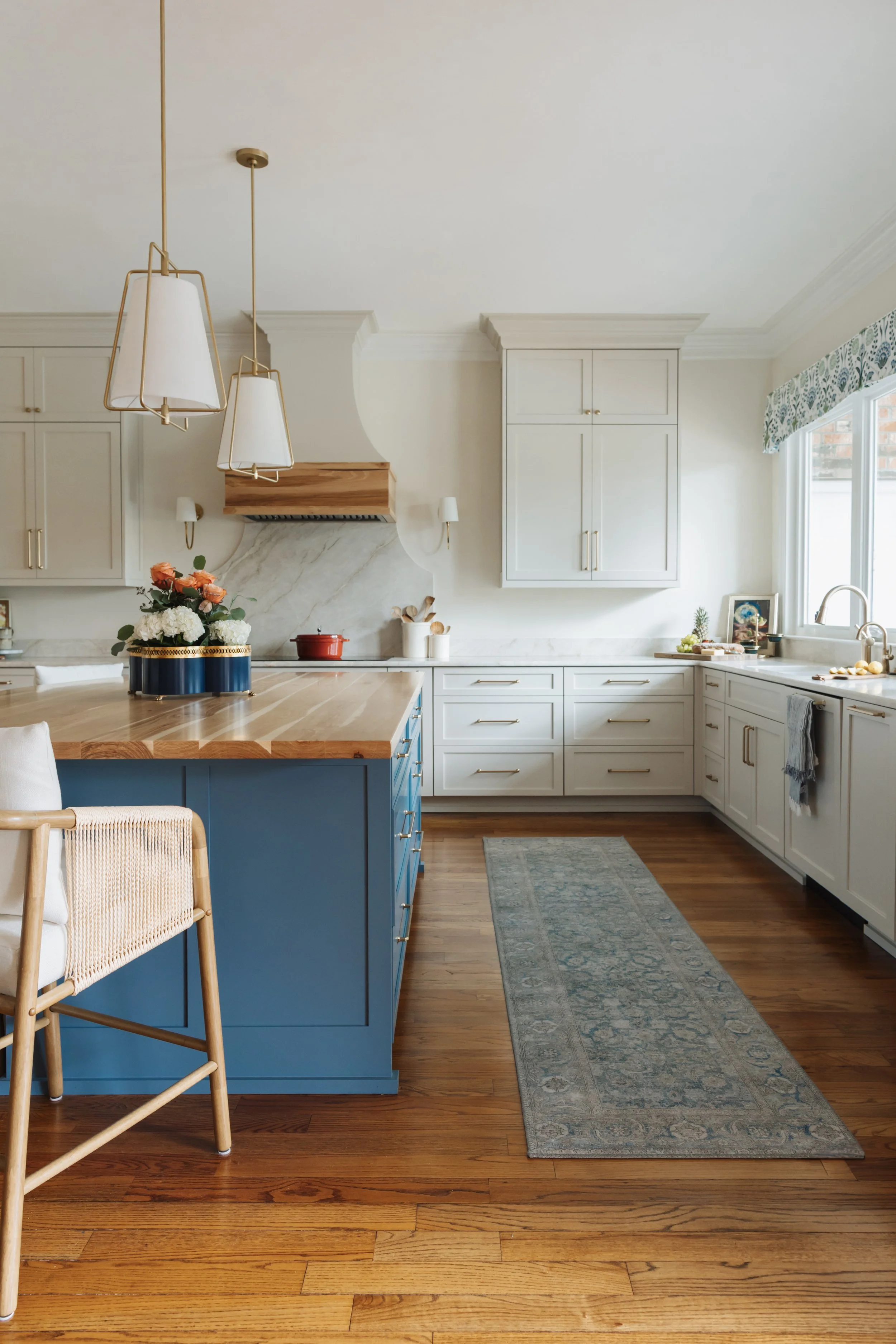 The custom kitchen island is painted a saturated blue, grounding the space and creating a bold focal point against the surrounding light cabinetry. A thick butcher block countertop introduces warmth and natural wood grain, inviting gathering, prep, a