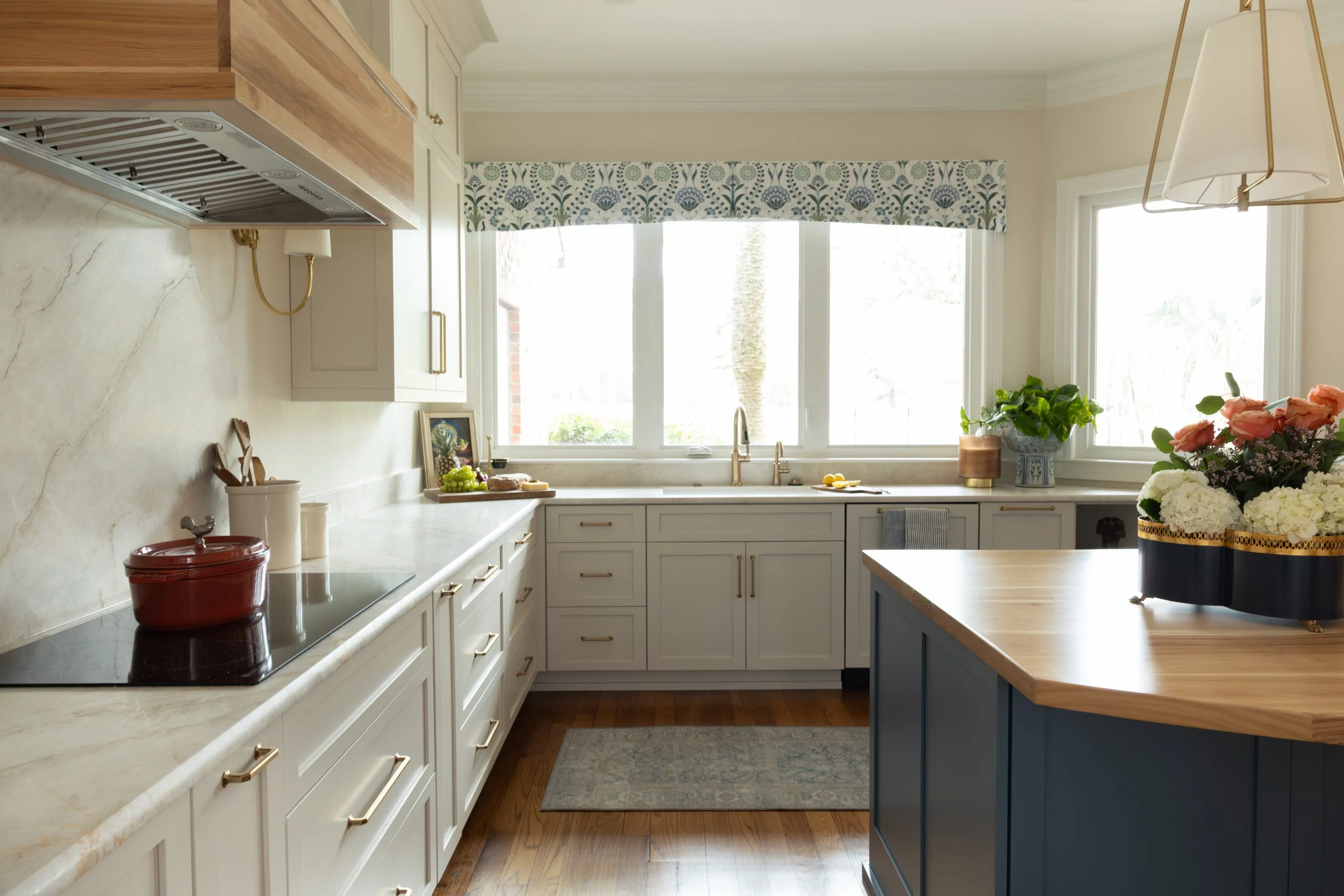 An undermount kitchen sink sits beneath the window, framed by pale stone countertops that reflect light throughout the room. The streamlined faucet adds a subtle shine while maintaining a clean, functional look. A large kitchen window above the sink 