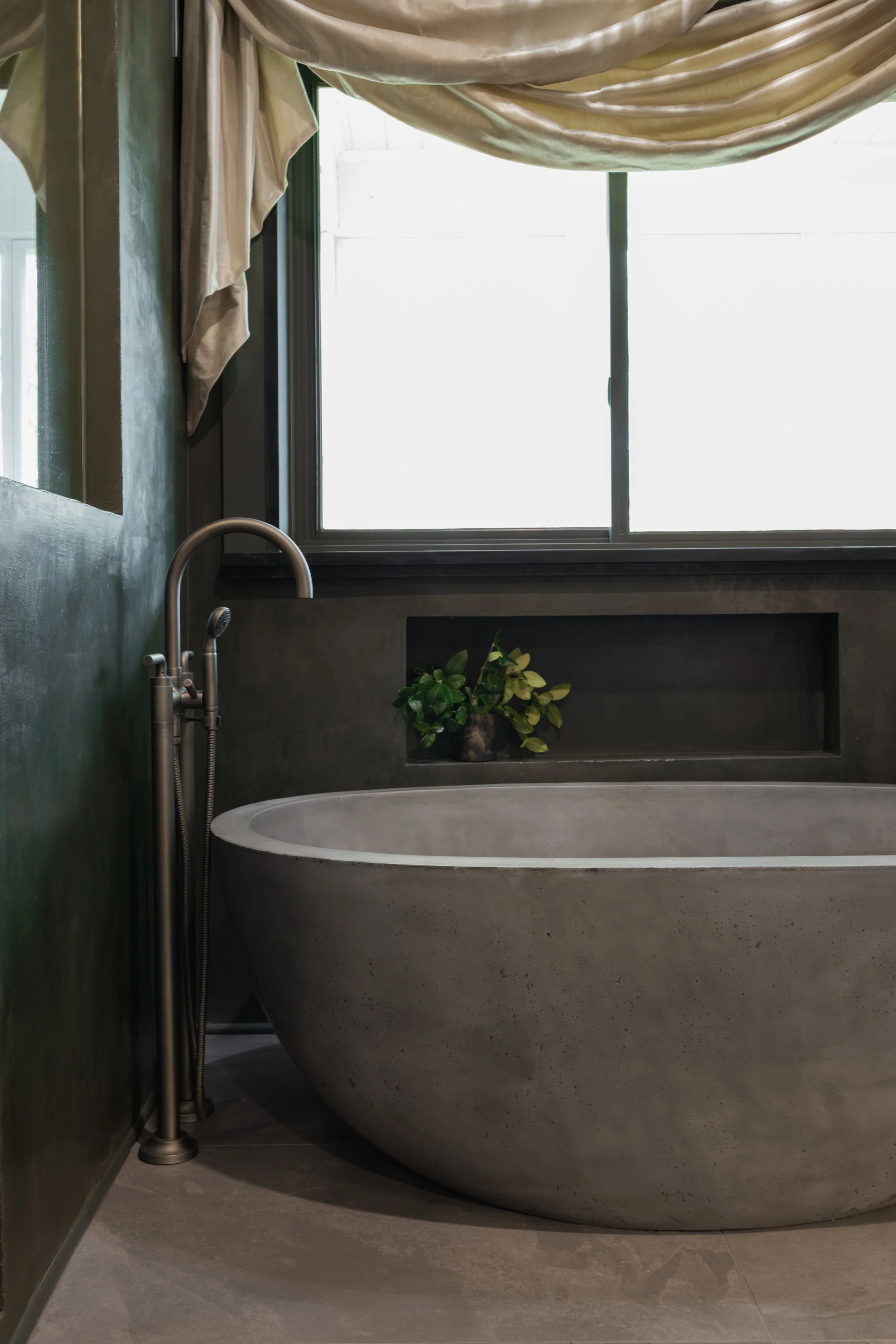 The sculptural stone soaking tub anchors the room, its soft curves and matte finish creating a calm focal point against the moody, shadowed walls.