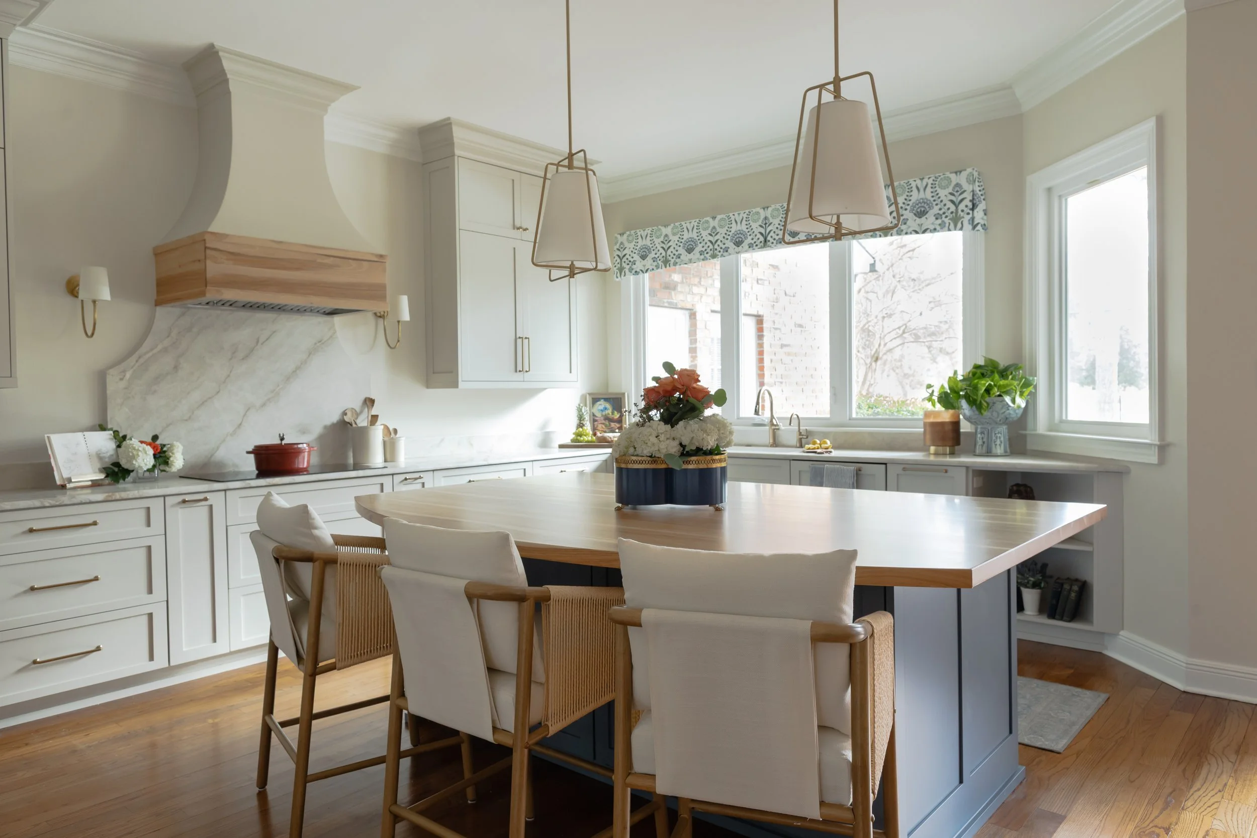 The custom kitchen island is painted a saturated blue, grounding the space and creating a bold focal point against the surrounding light cabinetry. A thick butcher block countertop introduces warmth and natural wood grain, inviting gathering, prep, a
