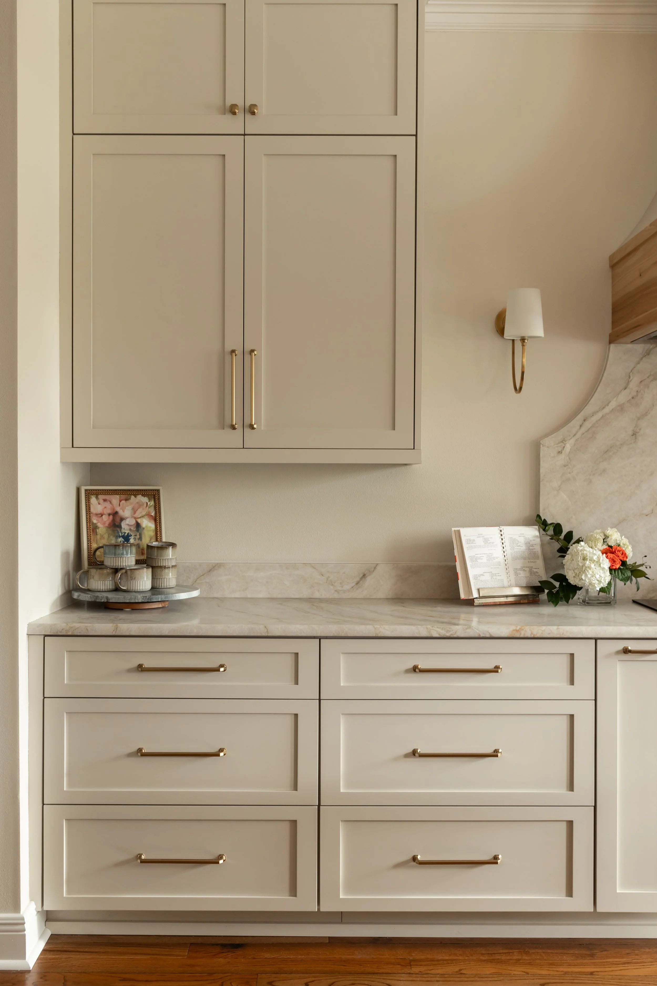 Shaker-style kitchen cabinets in a soft white finish wrap the space, offering a timeless backdrop with crisp lines and classic proportions. Full-height uppers emphasize the ceiling height and contribute to the kitchen’s bright, airy feel. Sculptural 