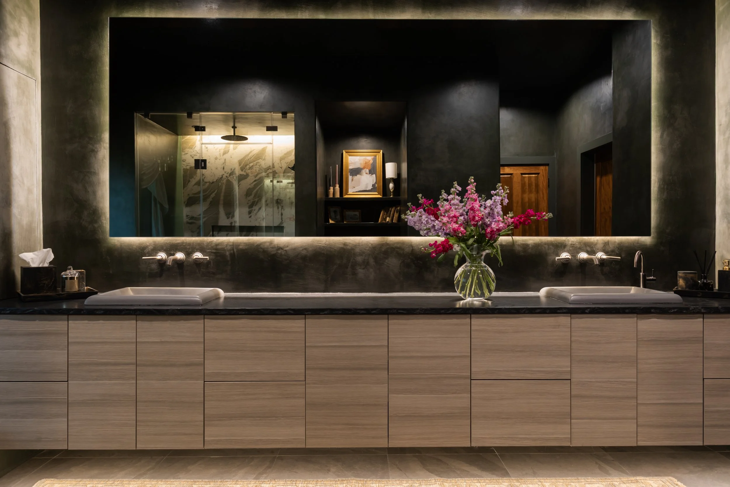 The modern bathroom vanity showcases warm wood cabinetry, a streamlined countertop sink, and a large wall-mounted mirror with integrated lighting, combining functionality and contemporary style to elevate the overall bathroom renovation.