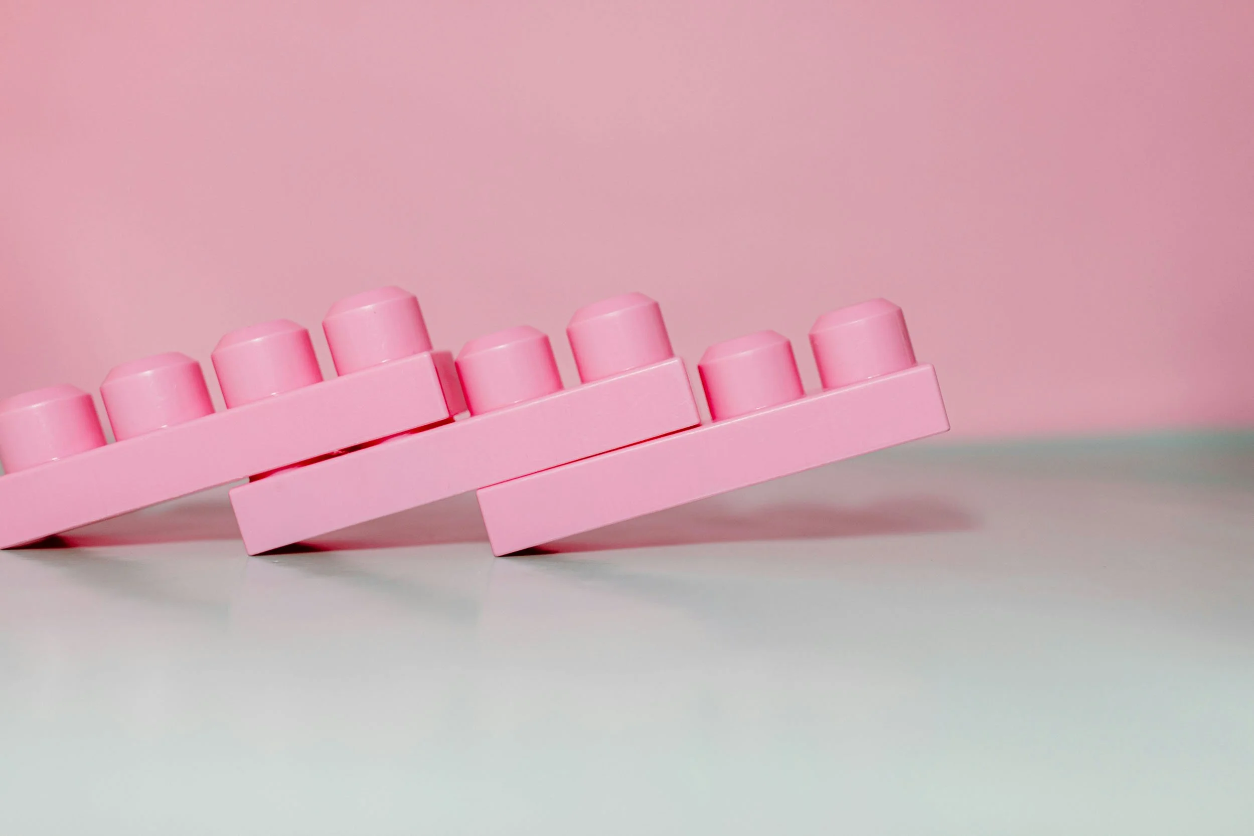 Pink plastic toy building blocks arranged in a row on a white surface with a pink background.