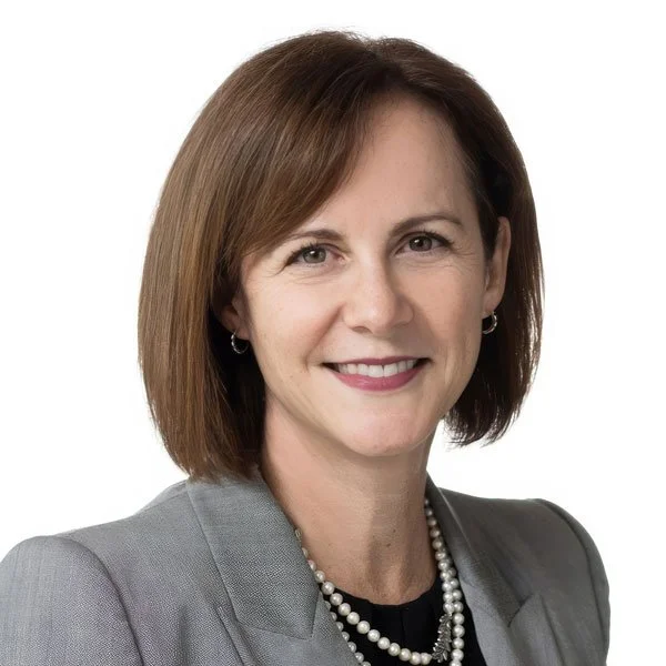 Professional woman with brown hair, wearing a gray blazer and pearl necklace, smiling against a white background.