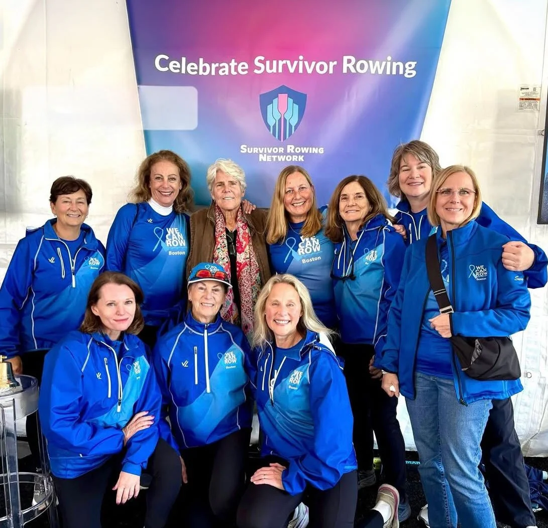 Group of women wearing blue jackets gathered in front of a banner that reads 'Celebrate Survivor Rowing' with the Survivor Rowing Network logo, during a rowing event in Boston.