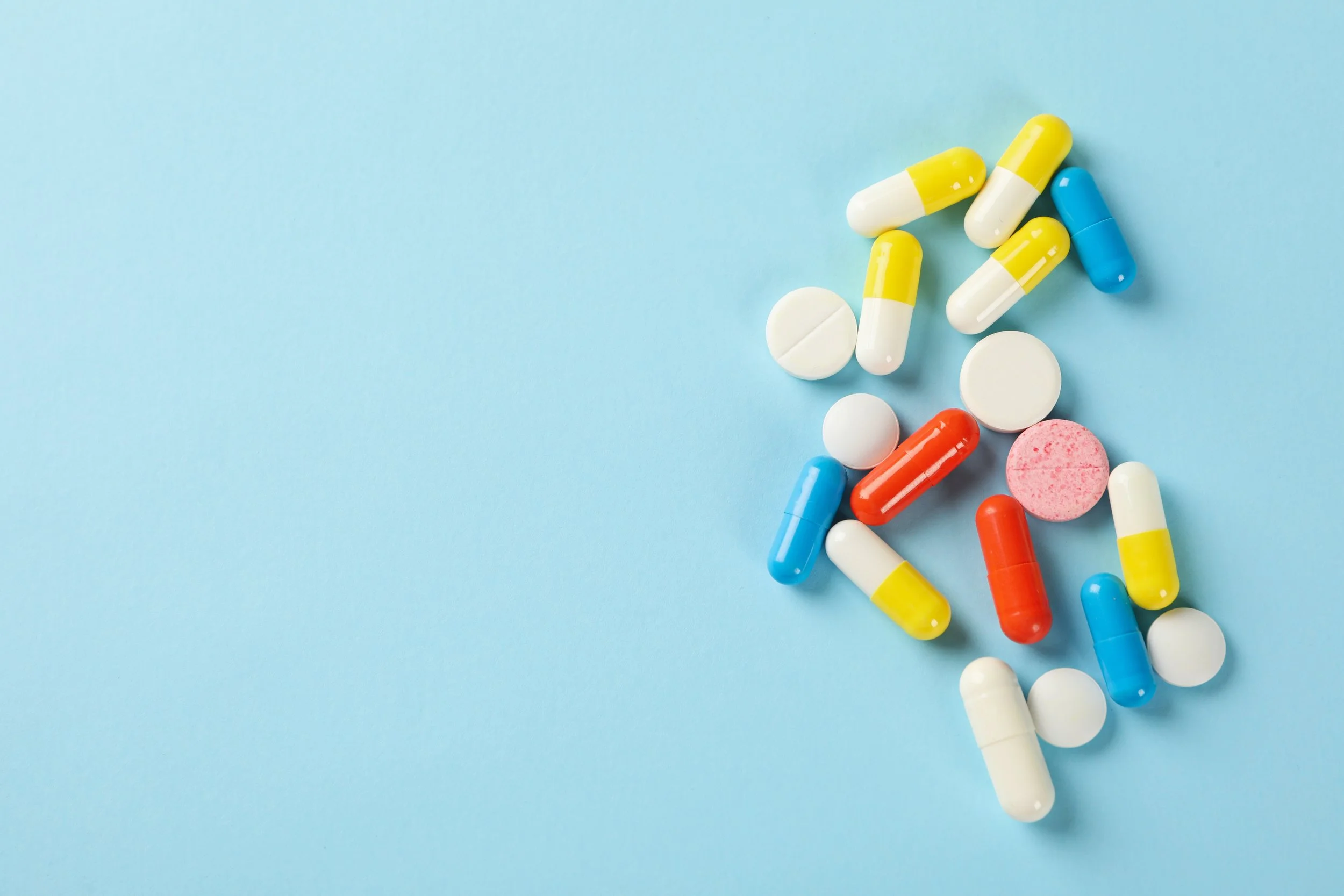 Assorted pills and tablets scattered on a light blue background.