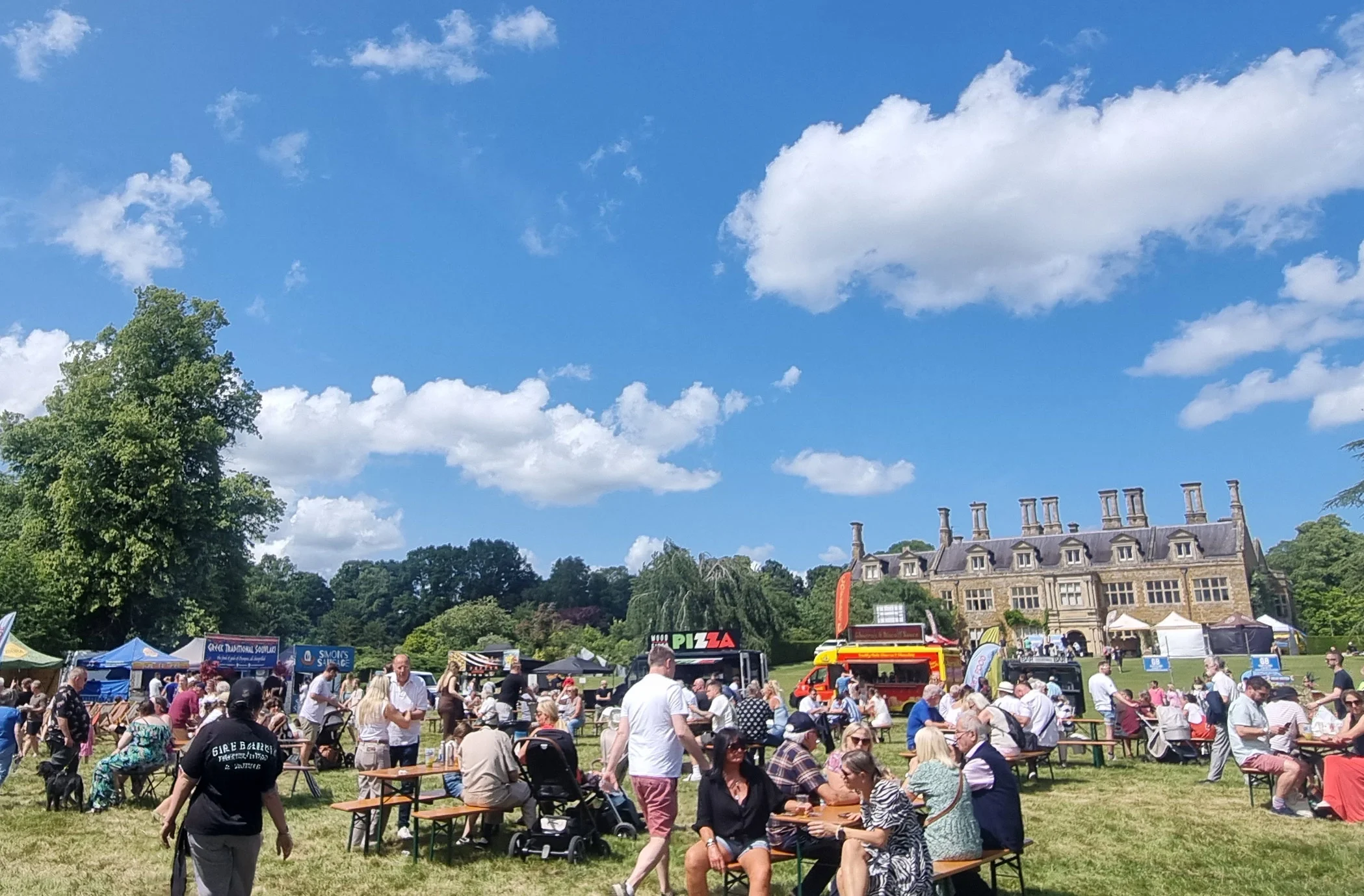 People sat at tables in manor garden at festival.