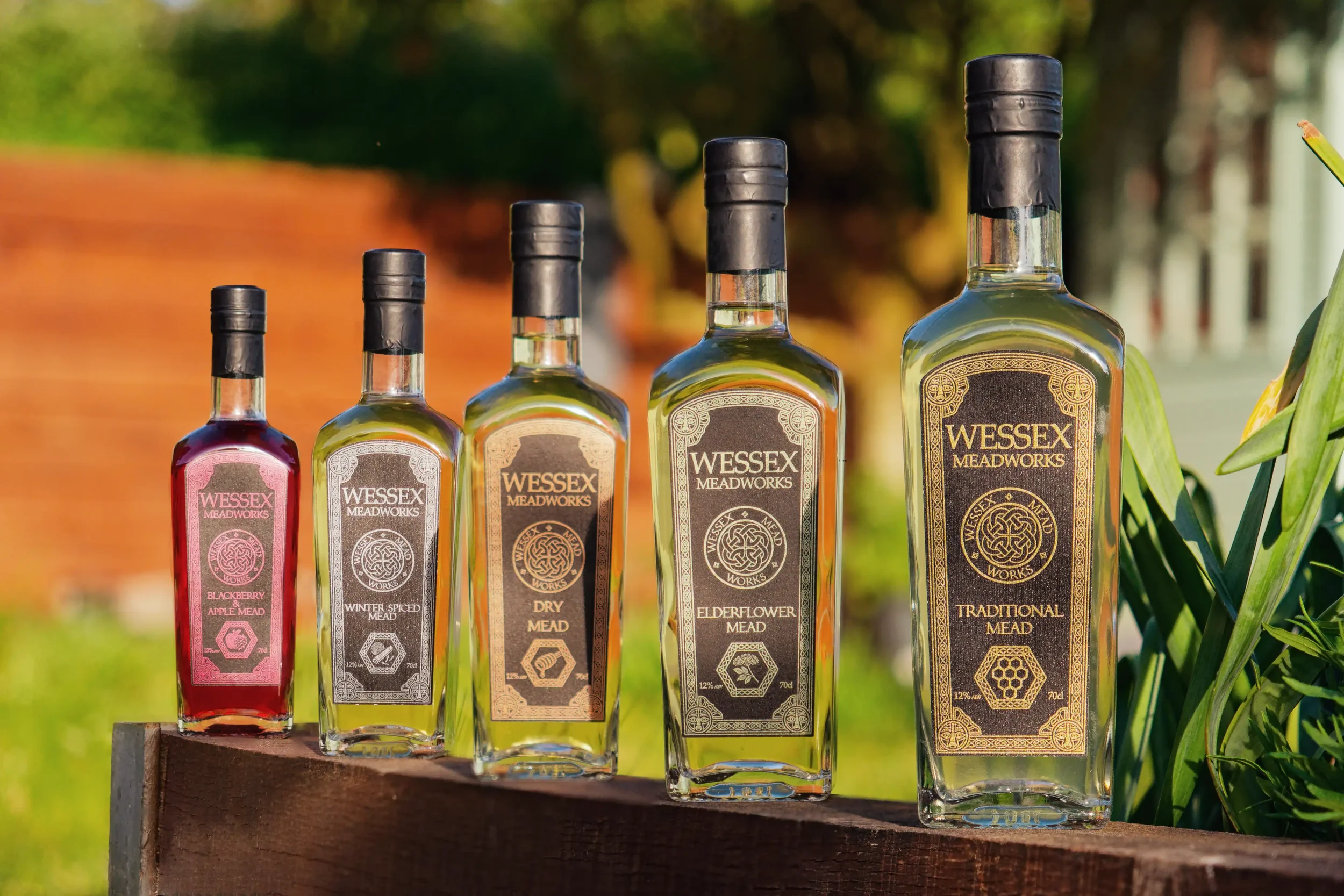 Wessex Meadworks bottles of mead, various flavours, on wood wall in a line, garden.