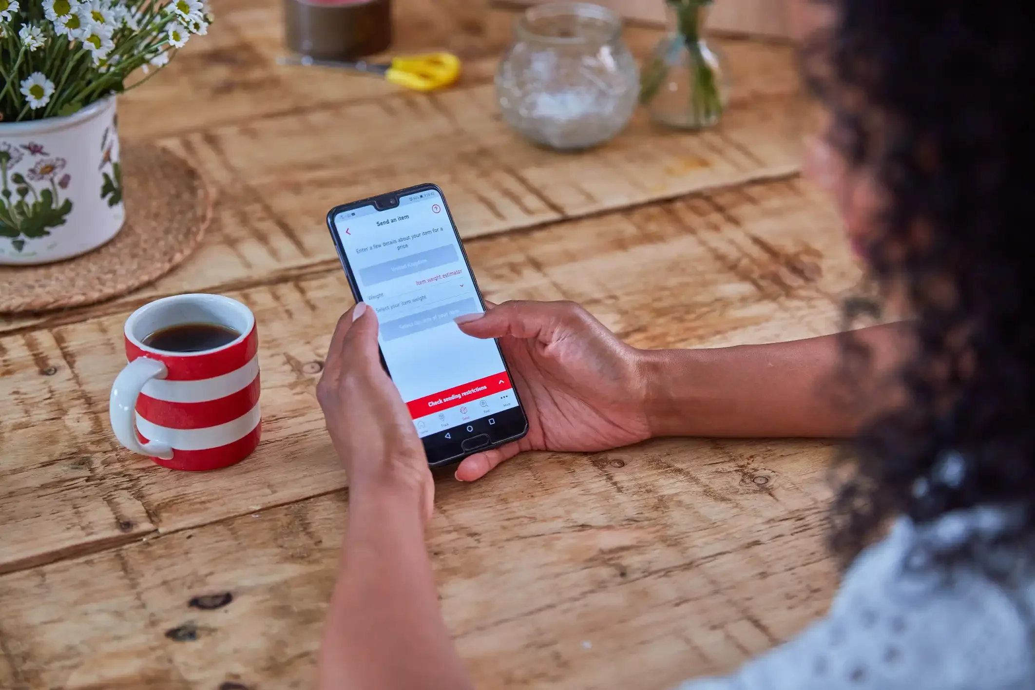 Woman sat at table looking at Royal Mail tracking app on phone.