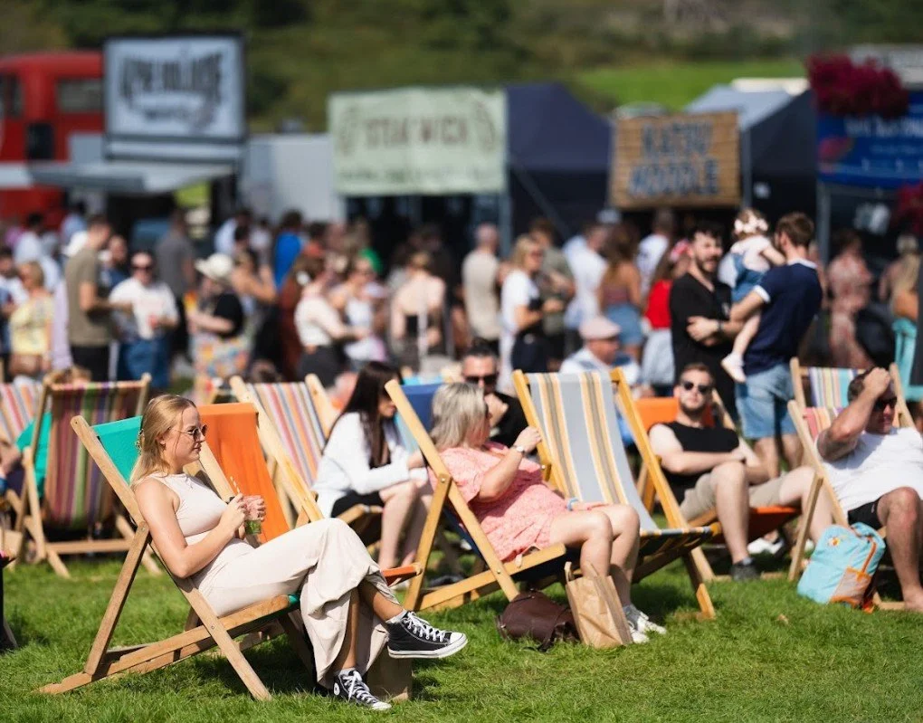 Summer, crowd sat in foldable deckchairs near festival stalls